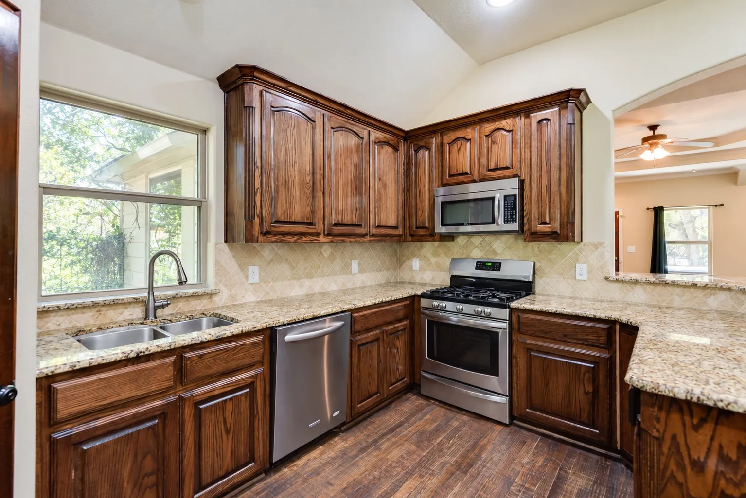 Kitchen featuring wood-finish flooring, stainless steel appliances, granite countertops, wood cabinetry, and a tile backsplash