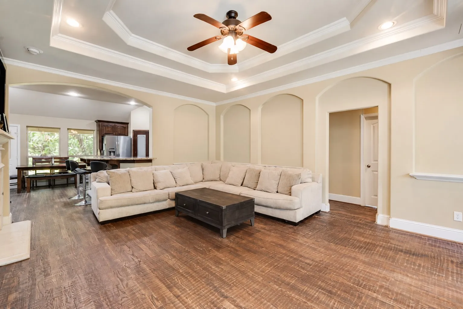 Tray ceiling with crown molding and recessed lighting, wood-finish flooring, arched wall niches, and a white fireplace surround