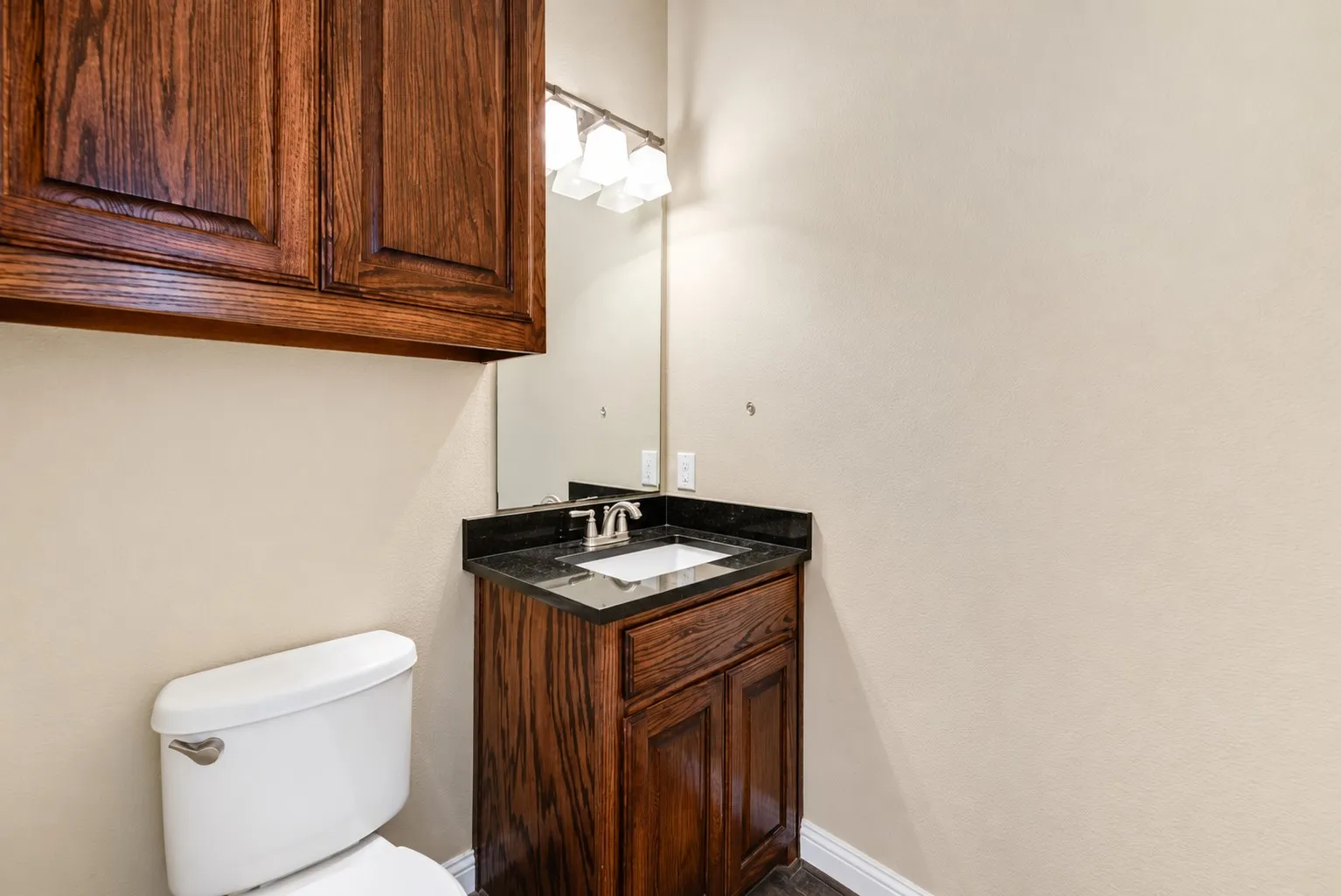 Rich wood-finish cabinetry, dark stone countertop, undermount sink, and wall-mounted vanity lighting