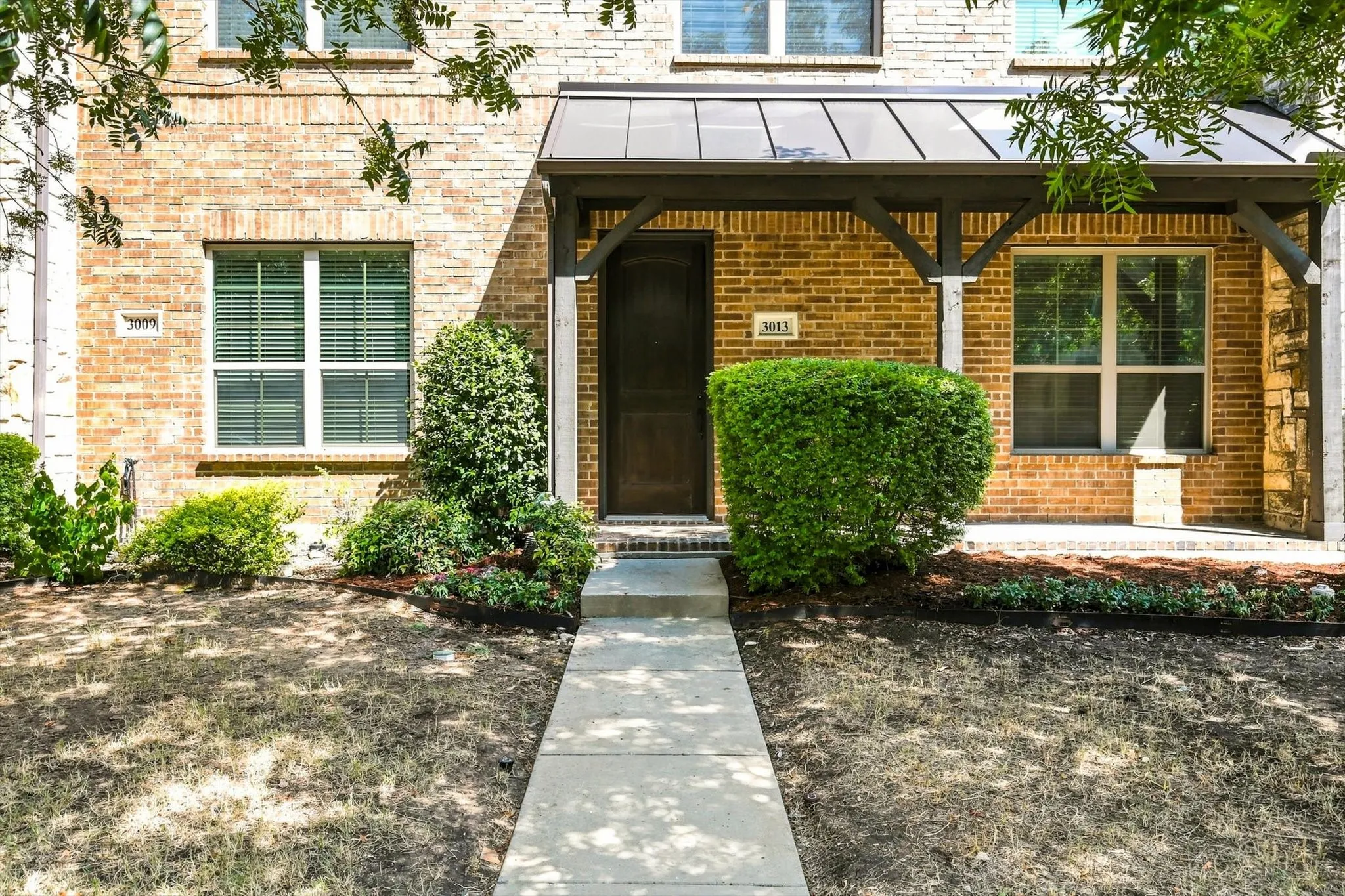 Charming brick townhome in the gated Villas at Stonegate community, shaded by mature trees with a welcoming covered entry.