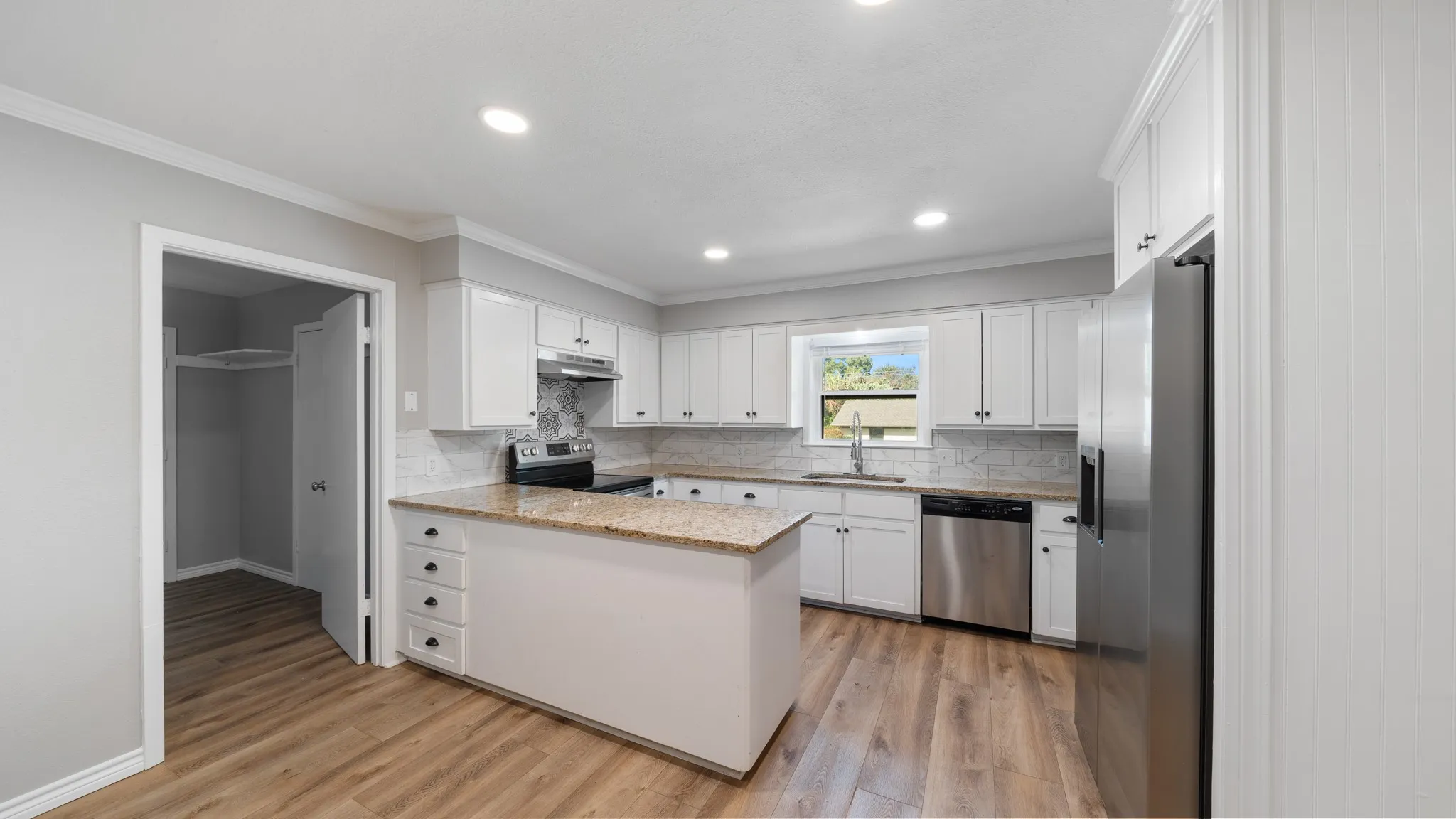 Kitchen featuring white cabinetry, a central island with drawers, stainless steel appliances, wood-finish flooring, and recessed lighting
