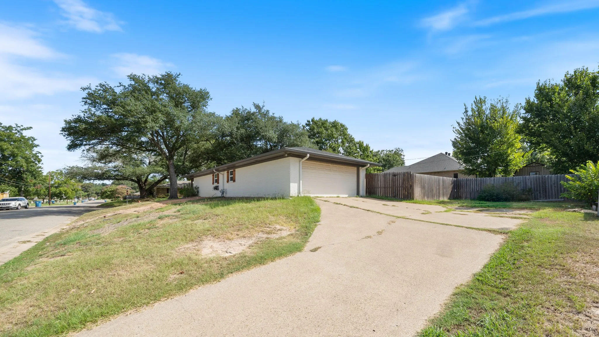 Concrete driveway with an attached two-car garage, white siding, and a partial wood fence