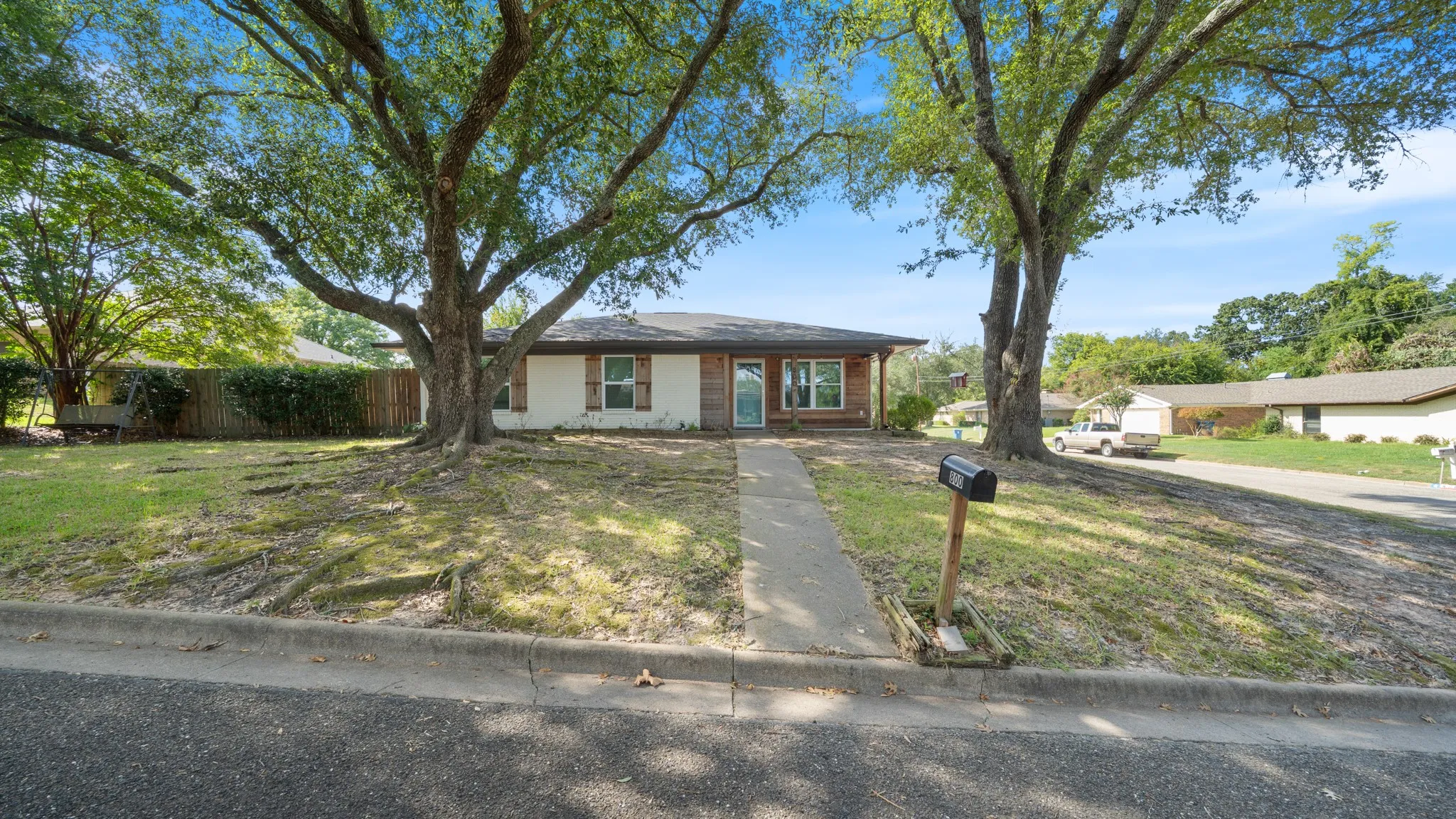 Ranch-style residence featuring a brick facade, a covered front porch, and mature trees in the front yard