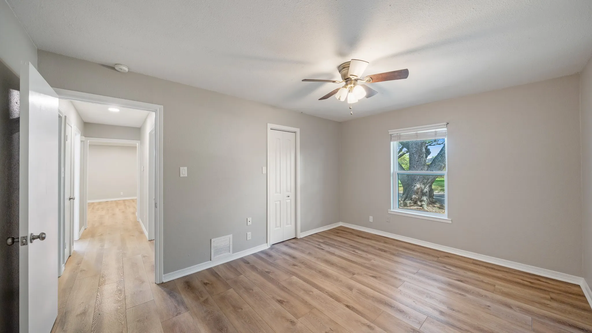 Wood-finish flooring, neutral wall color, ceiling fan with light fixture, window with roller shade, and white trim