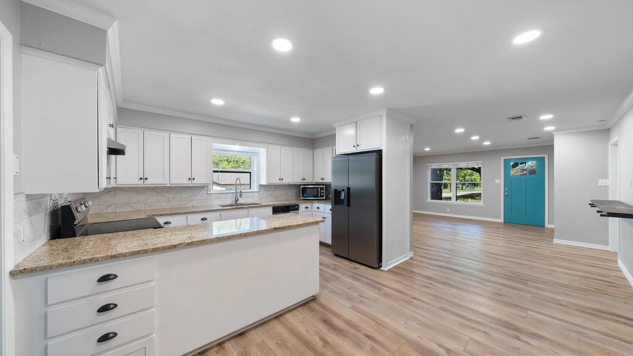 Open-concept living area featuring wood-finish flooring, recessed lighting, and a kitchen with white cabinetry and light-toned countertops