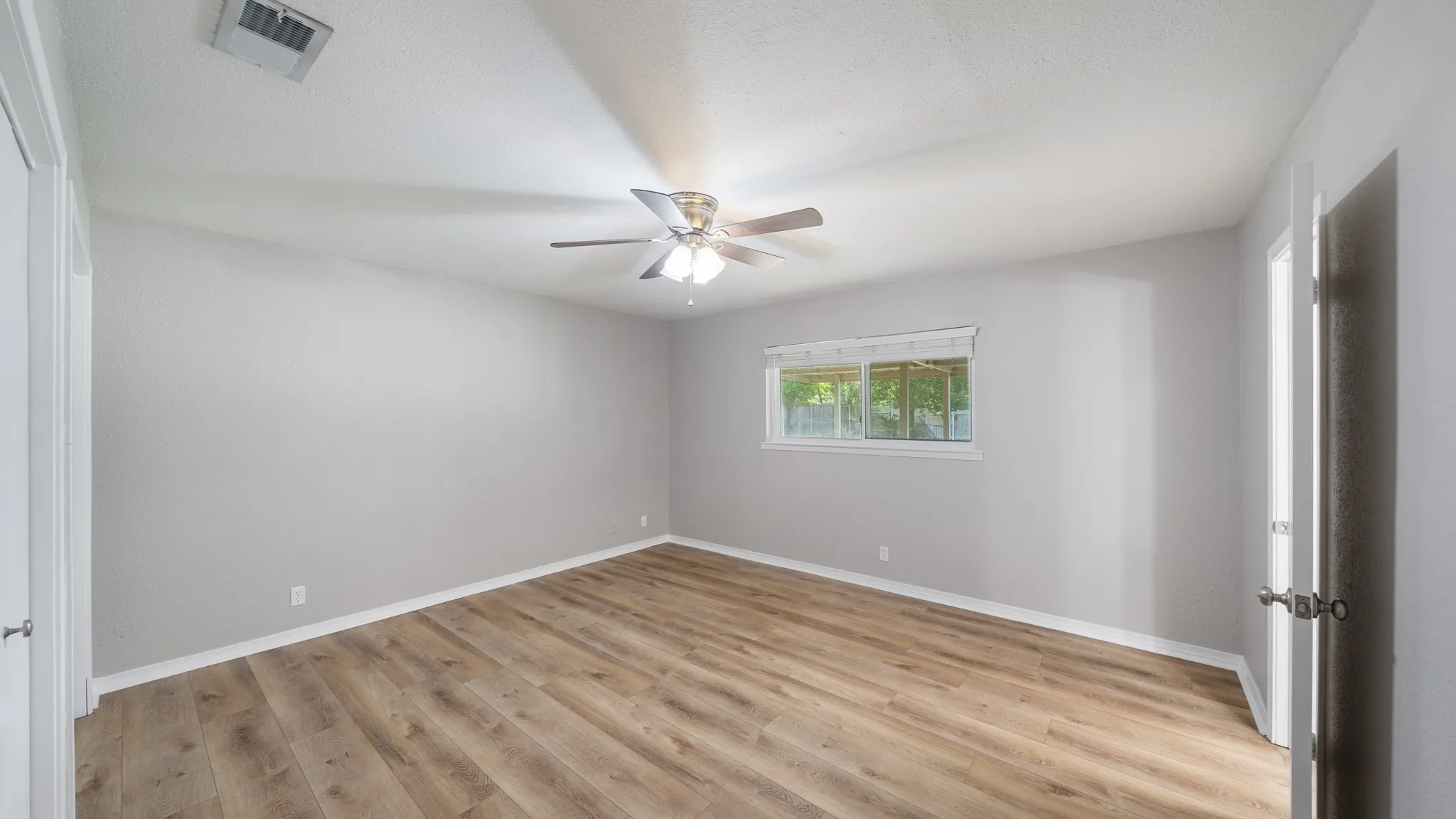 Wood-finish flooring, light gray wall tones, ceiling fan with integrated lighting, and white trim