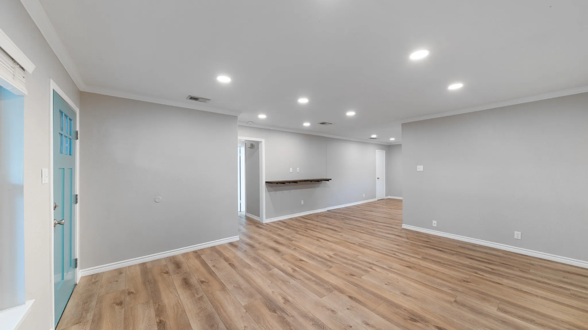 Recessed lighting, wood-finish flooring, light gray wall paint, white trim, and a built-in wall shelf