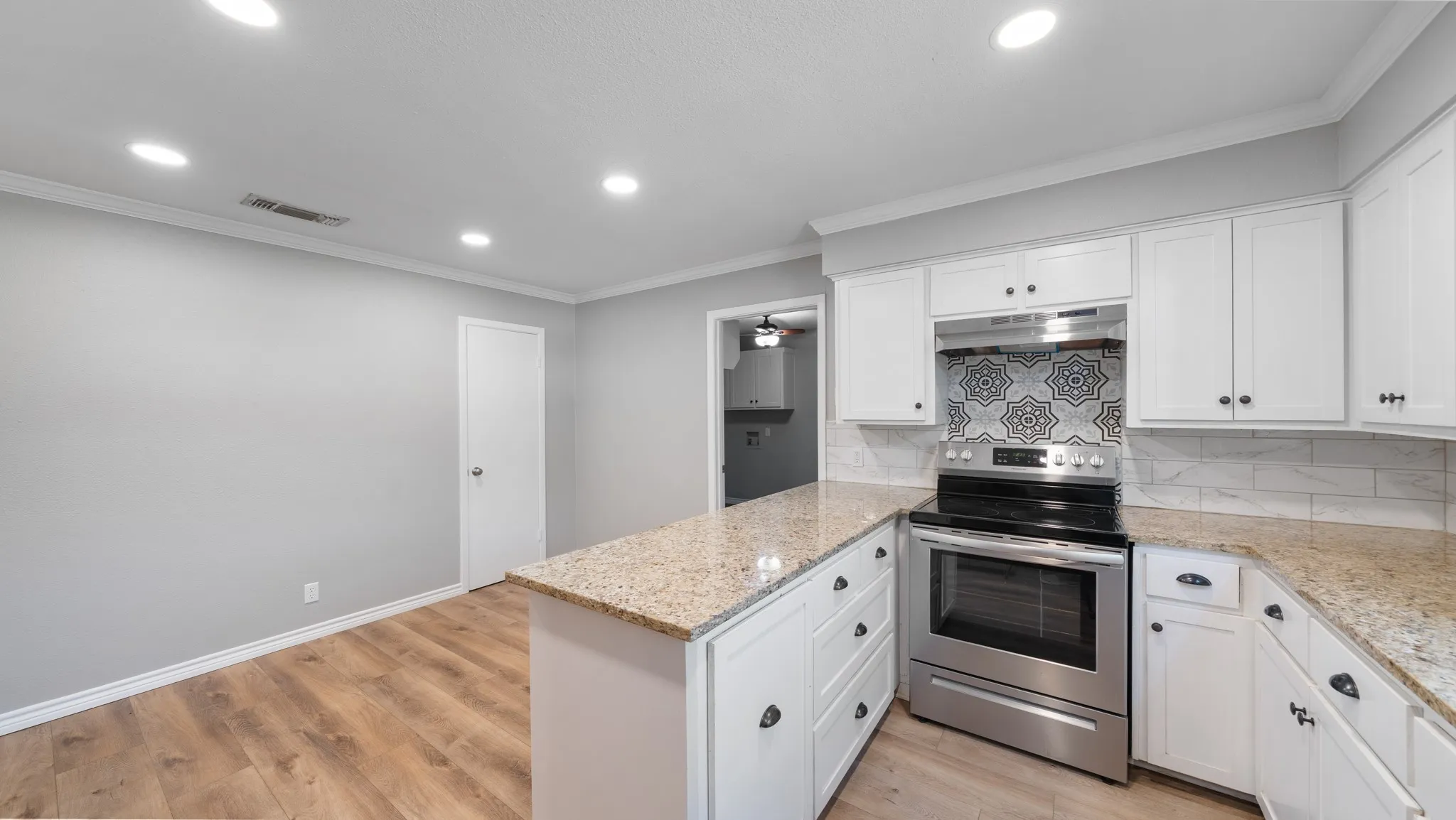 Modern kitchen featuring white cabinetry, granite countertops, stainless steel range, patterned tile backsplash, and wood-finish flooring