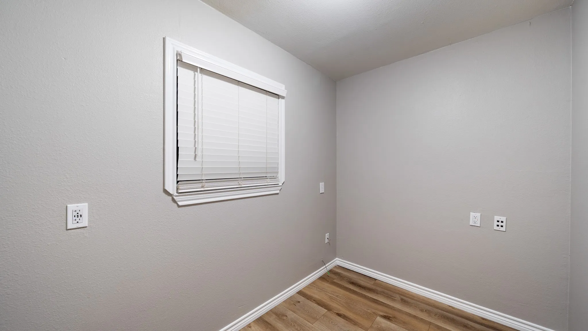 Room featuring wood-finish flooring, light gray walls, a window with white blinds, and white trim