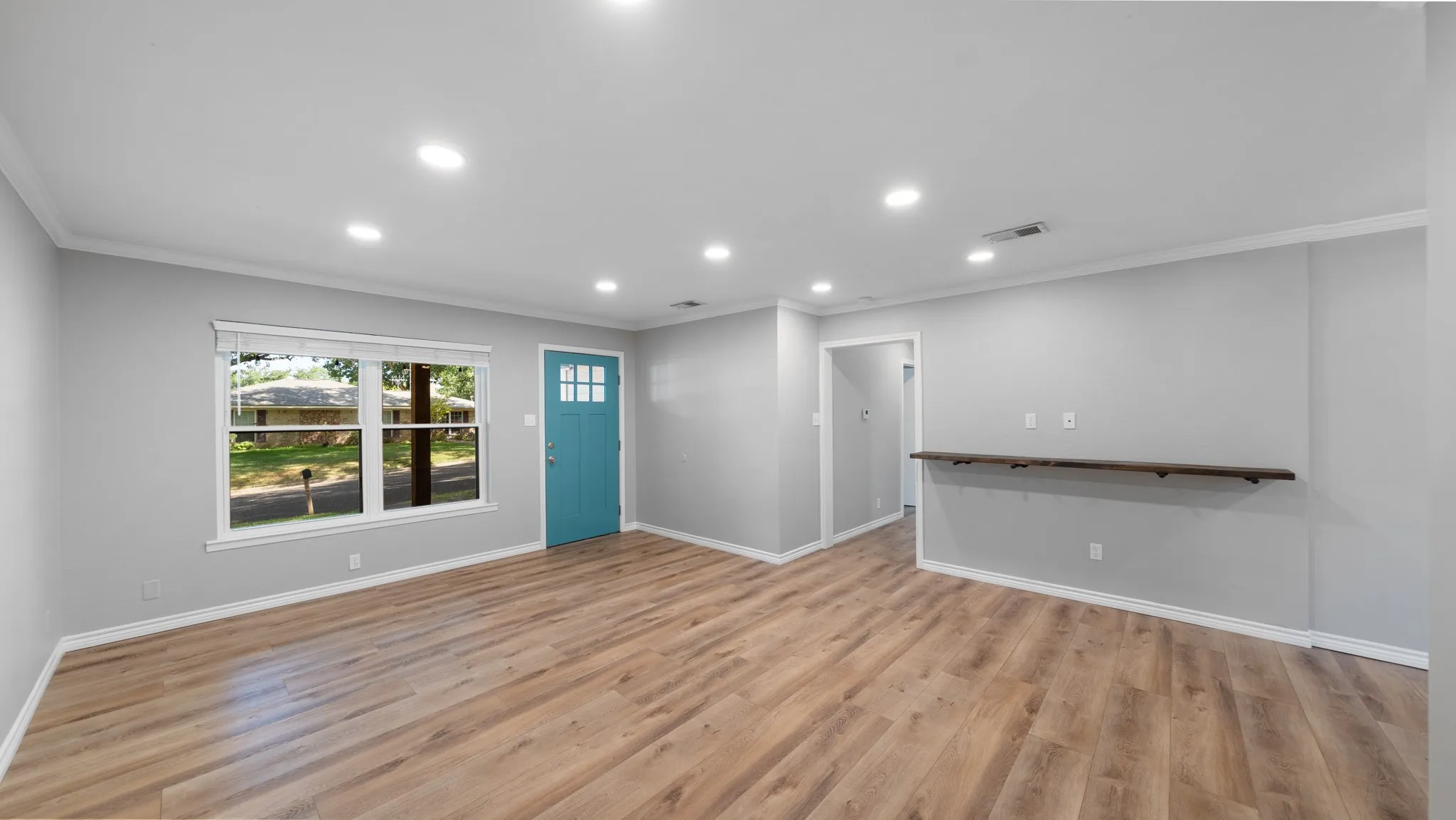 Recessed lighting, wood-finish flooring, light gray walls, built-in wall shelf, and a blue paneled door