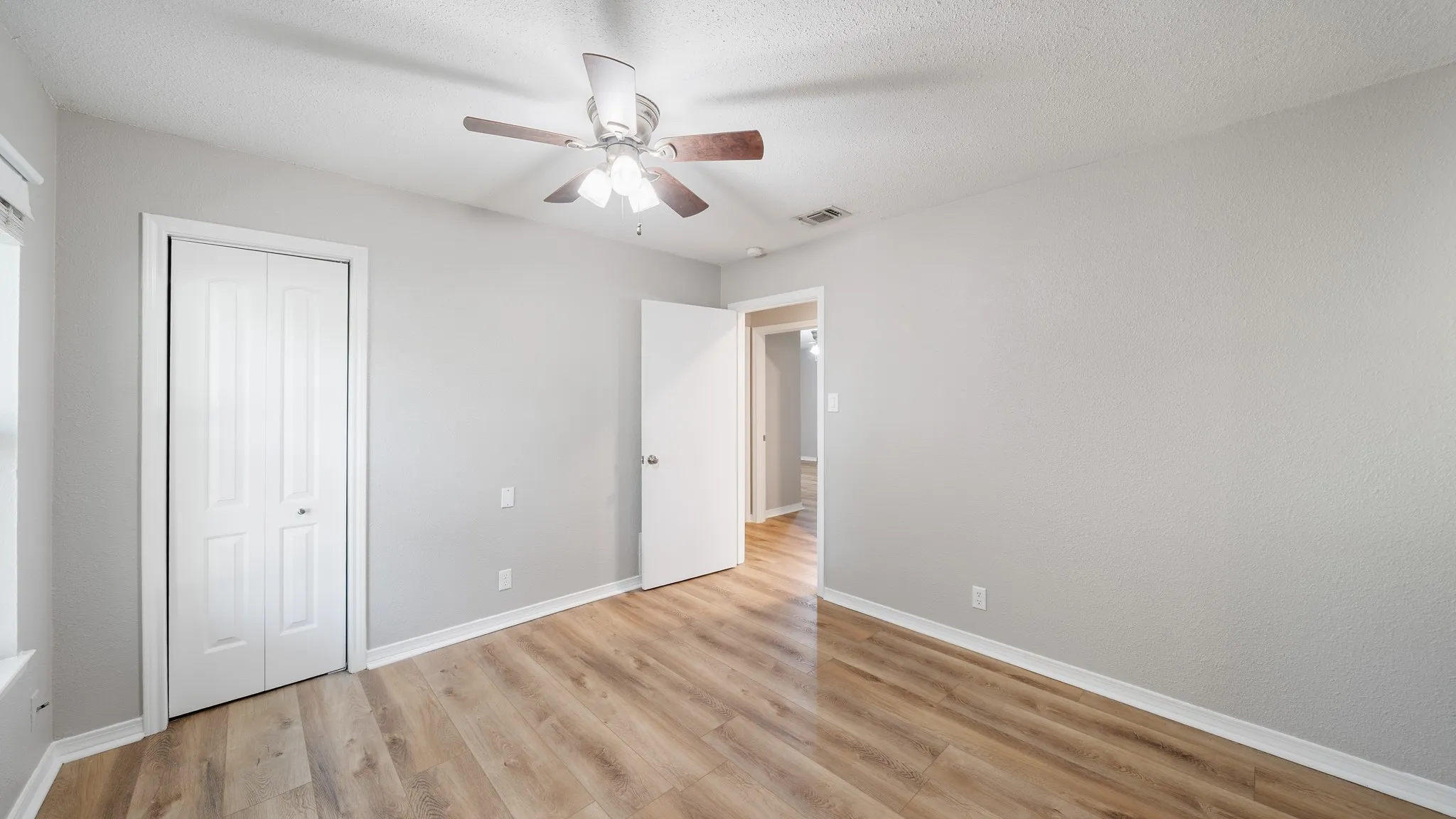 Neutral wall color, wood-finish flooring, ceiling fan with integrated lighting, bi-fold closet doors, and white trim