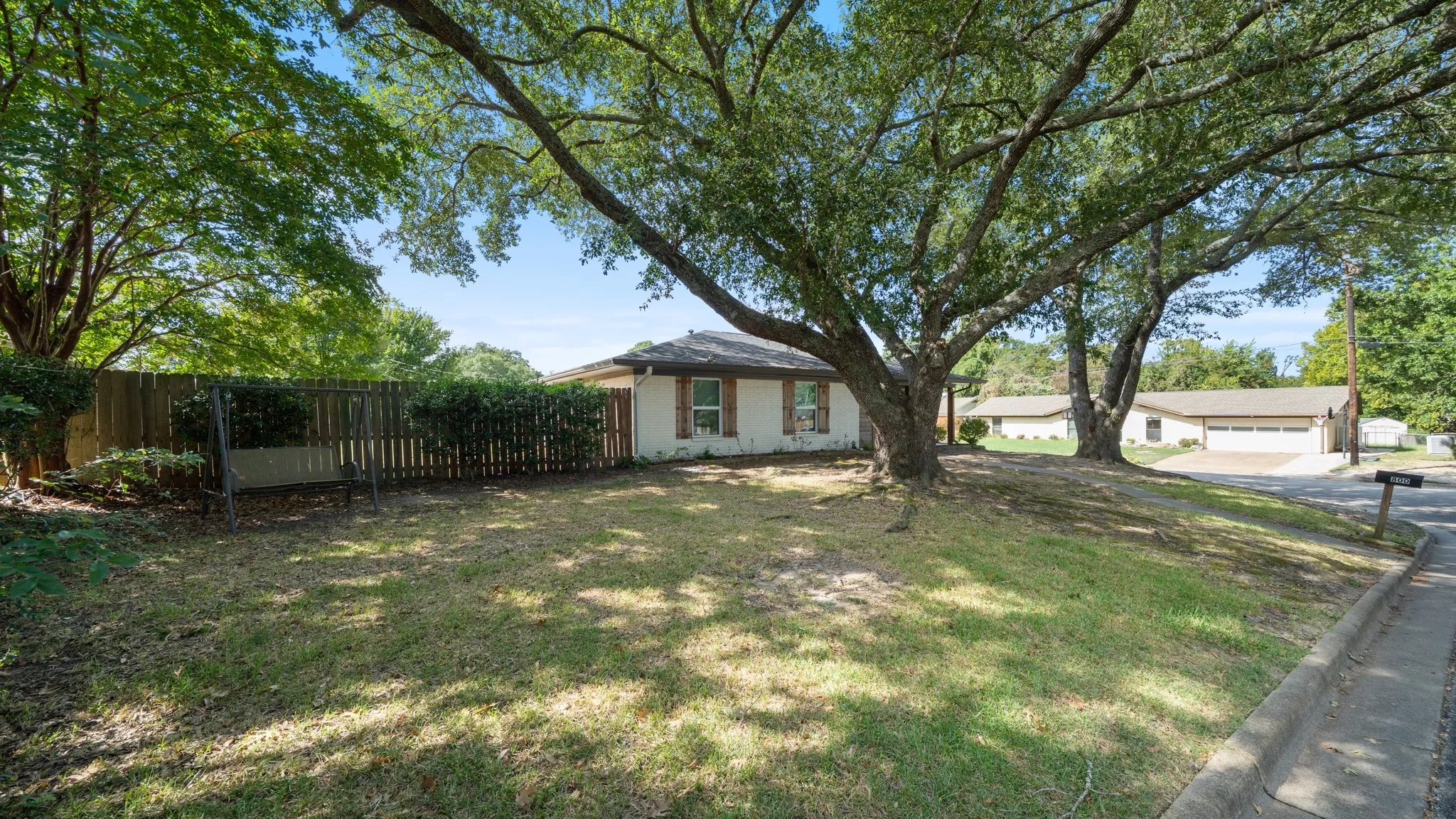 Expansive front yard with mature trees, established landscaping, and a sloped lawn
