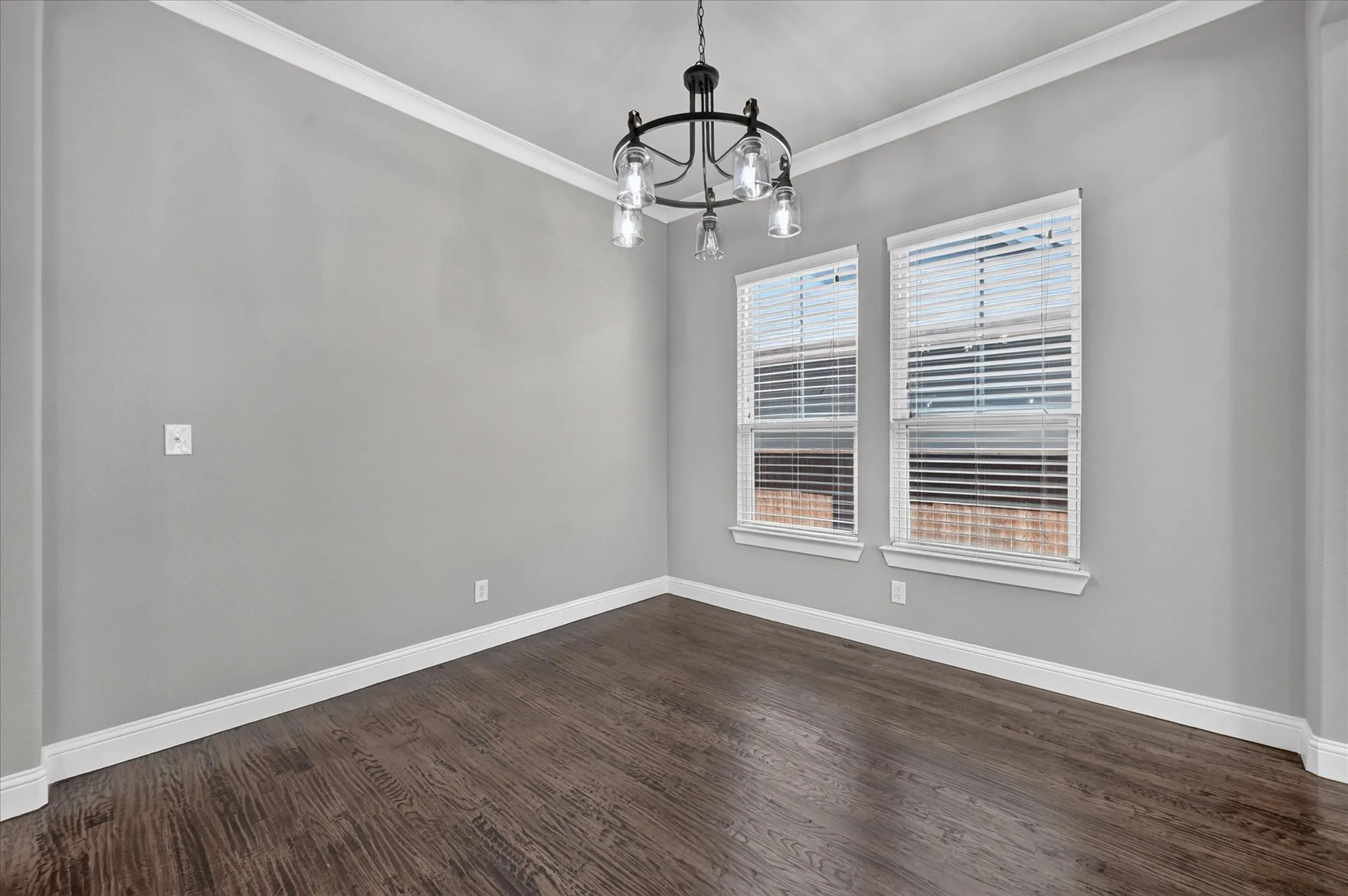Wood-finish flooring, crown molding, two windows with blinds, and an overhead chandelier with clear glass shades