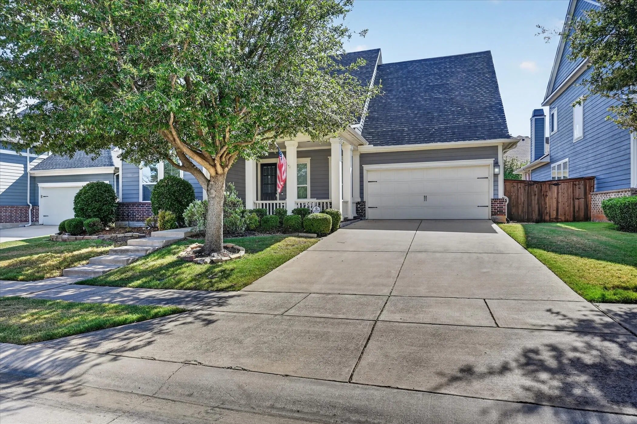 Gray siding exterior with white trim, a covered front porch with white columns, a two-car garage, and a concrete driveway