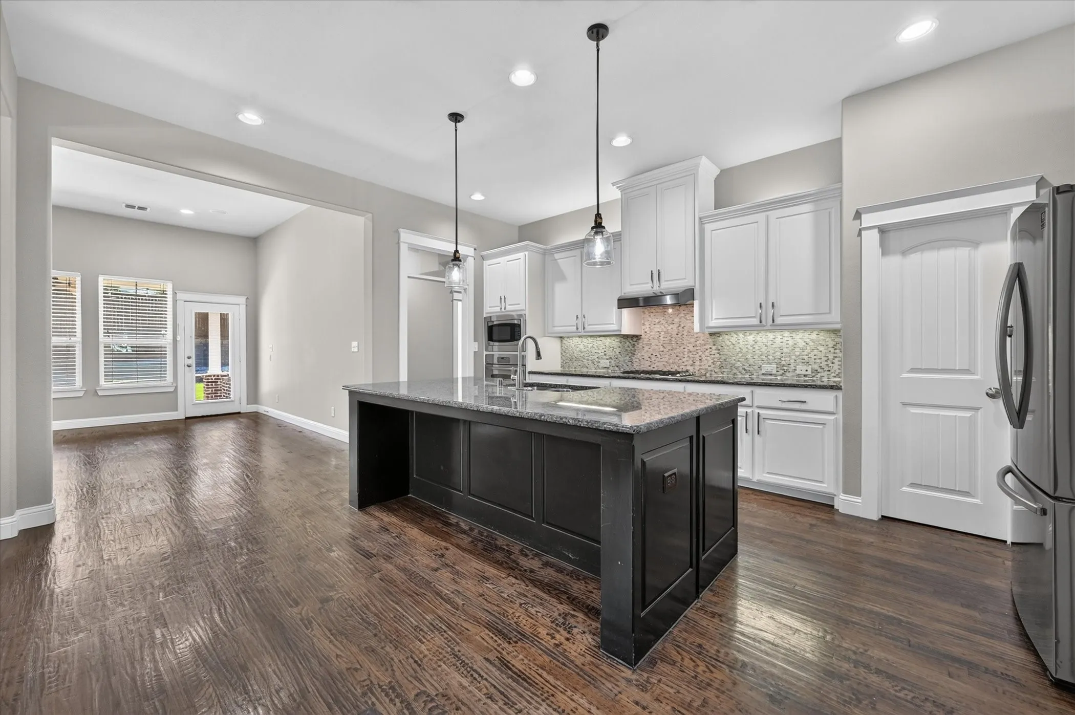 Kitchen featuring a dark wood-finish island with a light-toned countertop, white cabinetry, integrated stainless steel appliances, and wood-finish flooring