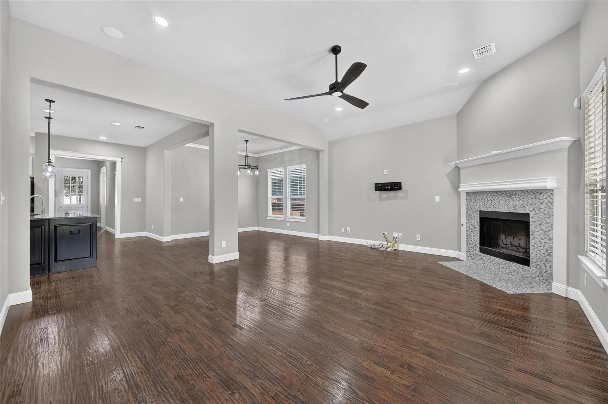 Vaulted ceiling with a black ceiling fan, wood-finish flooring, recessed lighting, fireplace with a tile surround and white mantel, and multiple windows with blinds