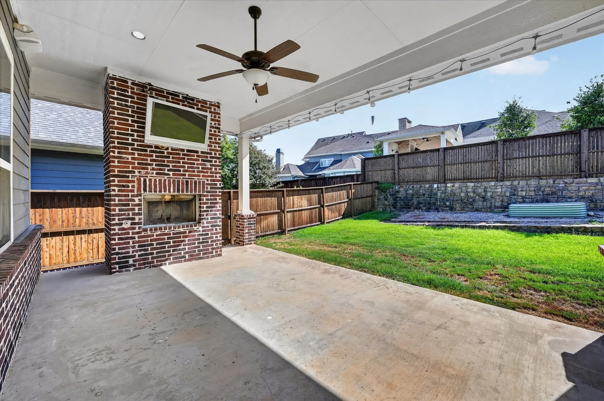 Covered patio featuring an integrated brick fireplace, concrete flooring, and a ceiling fan