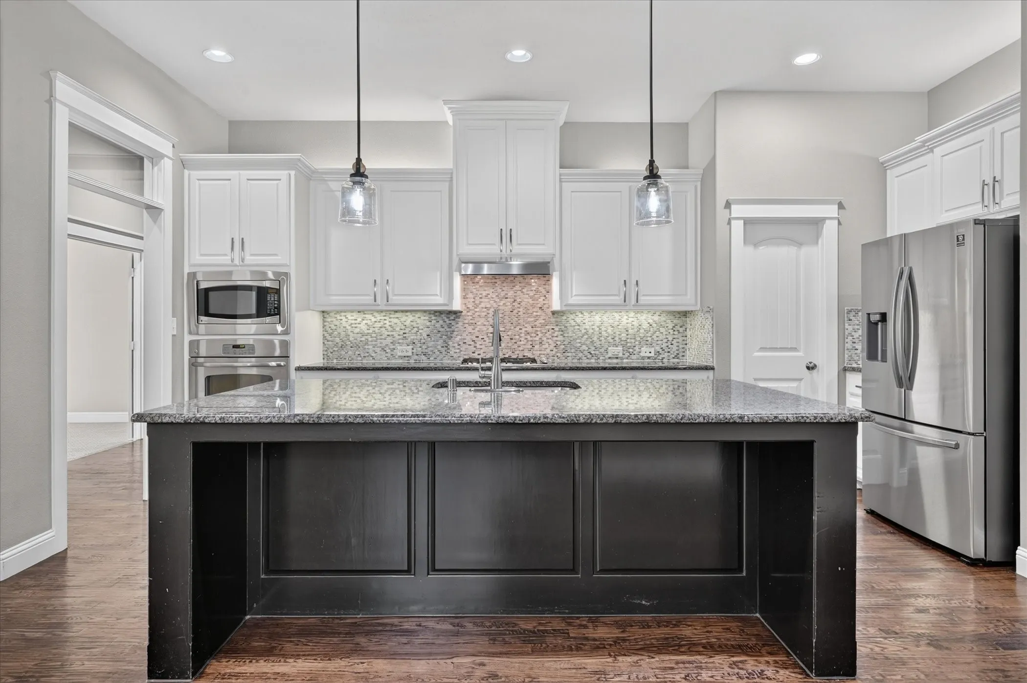 Central kitchen island with a dark finish and granite countertop, stainless steel appliances, white cabinetry, and recessed lighting