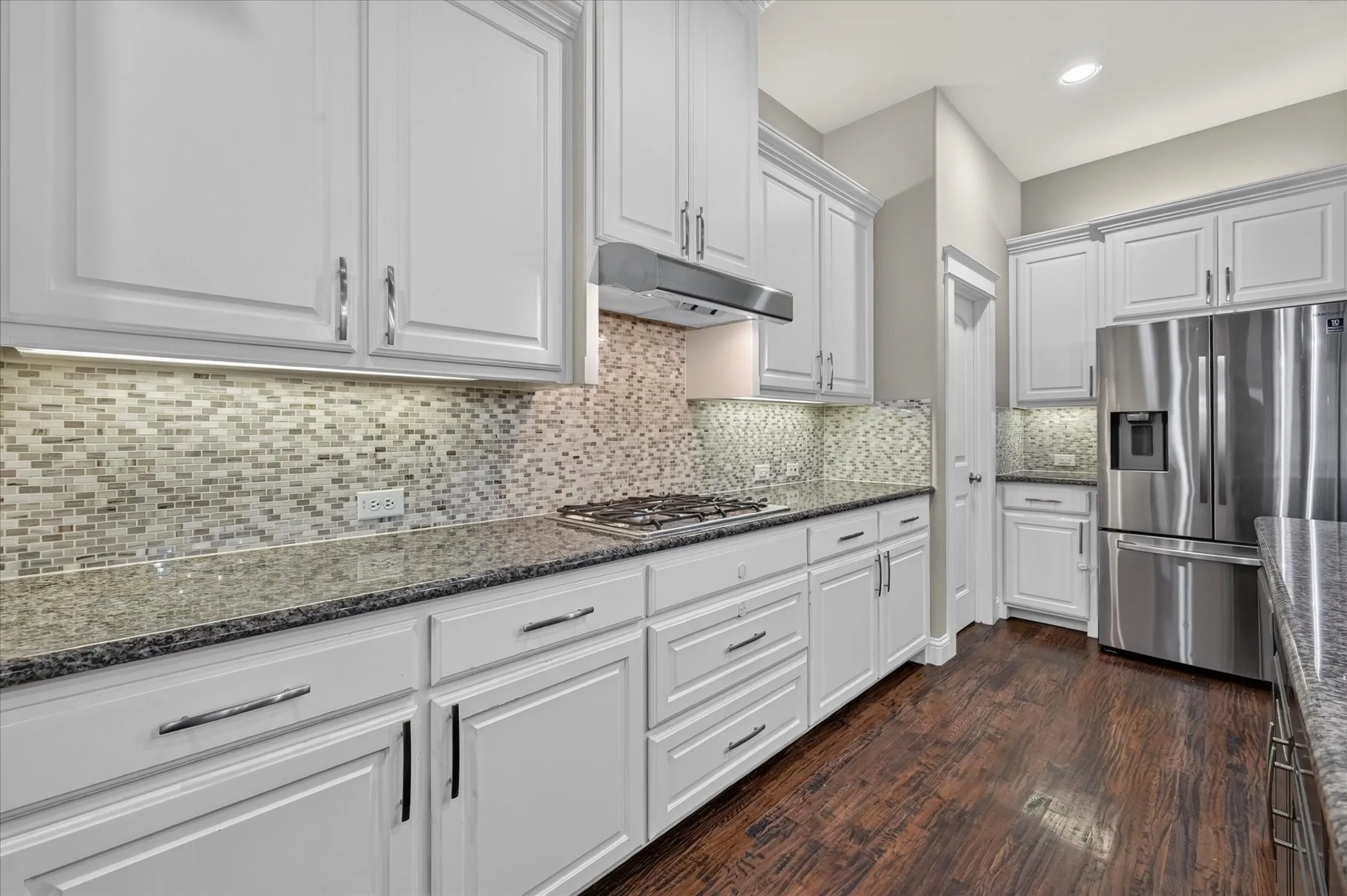 Kitchen featuring white cabinetry, granite countertops, stainless steel appliances, mosaic tile backsplash, and wood-finish flooring