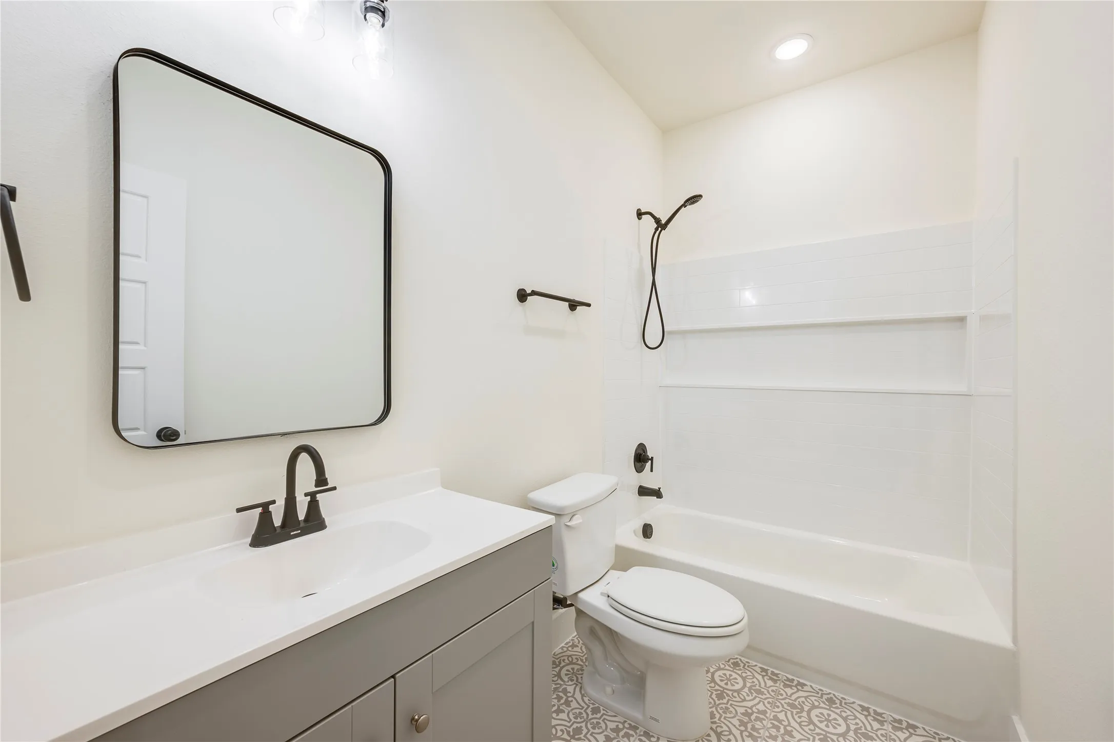 Bathroom featuring a vanity with a white countertop, matte black fixtures, a framed mirror, a tub-shower combination, and patterned floor tiling