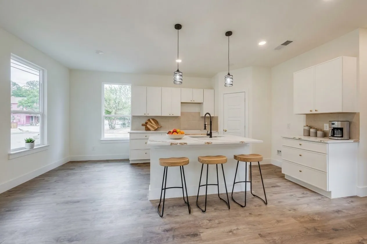 Open-concept kitchen with a large island, white cabinetry, integrated sink, and wood-finish flooring