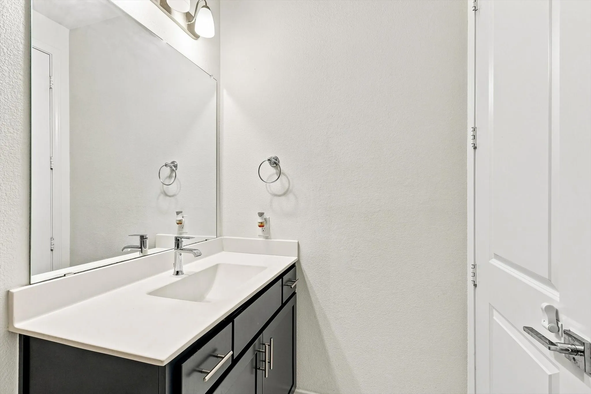 Vanity featuring an integrated rectangular sink with chrome faucet, a white countertop, and dark wood-finish cabinetry with chrome hardware