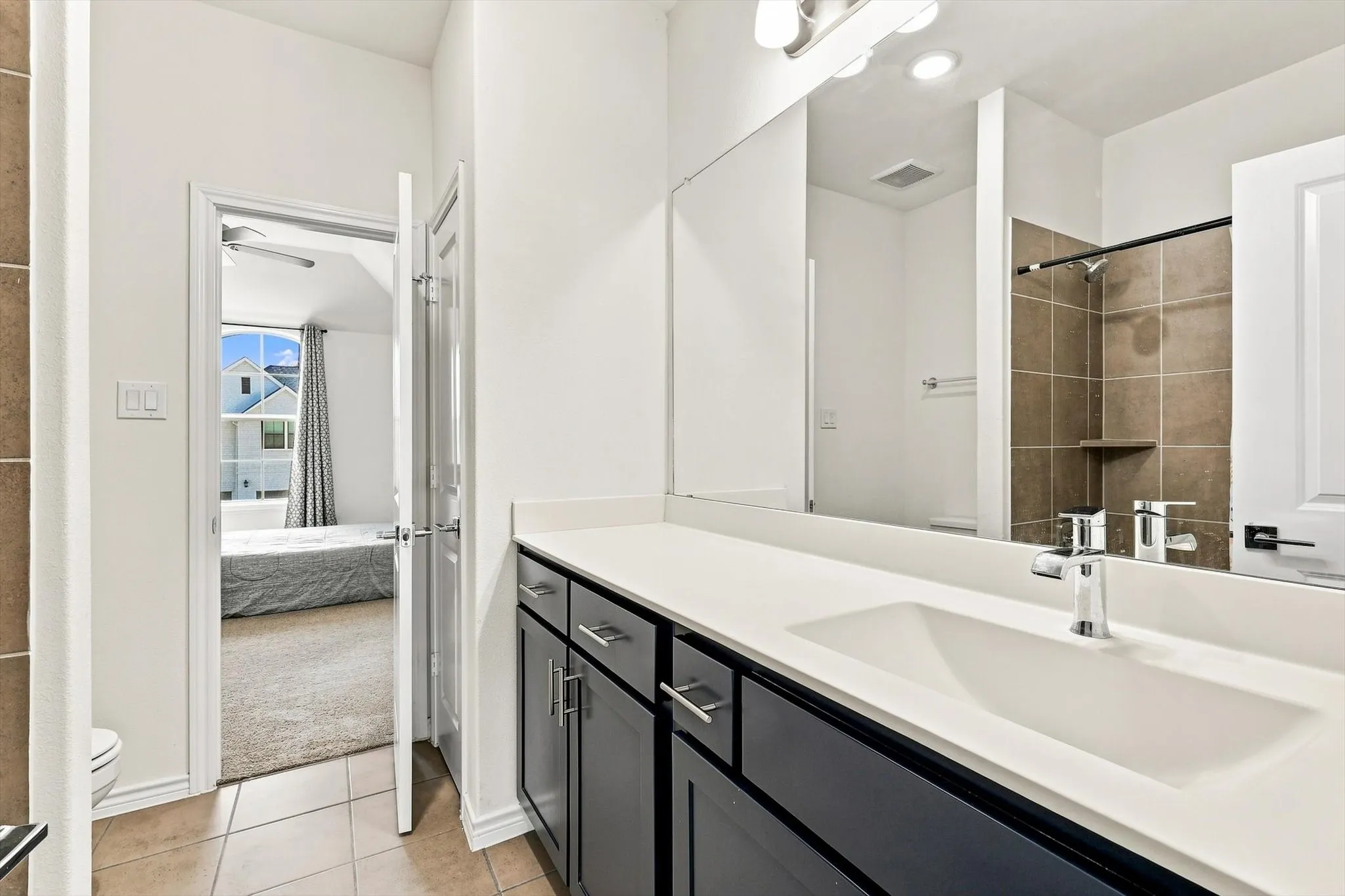 Dual-basin vanity with a white countertop and dark cabinetry, featuring a large wall-mounted mirror and chrome fixtures