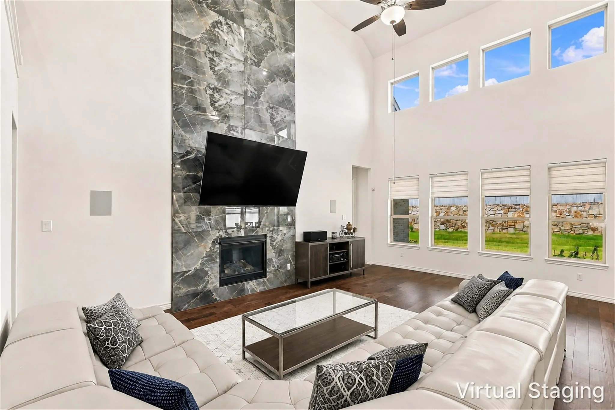 Vaulted ceilings with a ceiling fan, a fireplace with a full-height stone surround, wood-finish flooring, and multiple windows