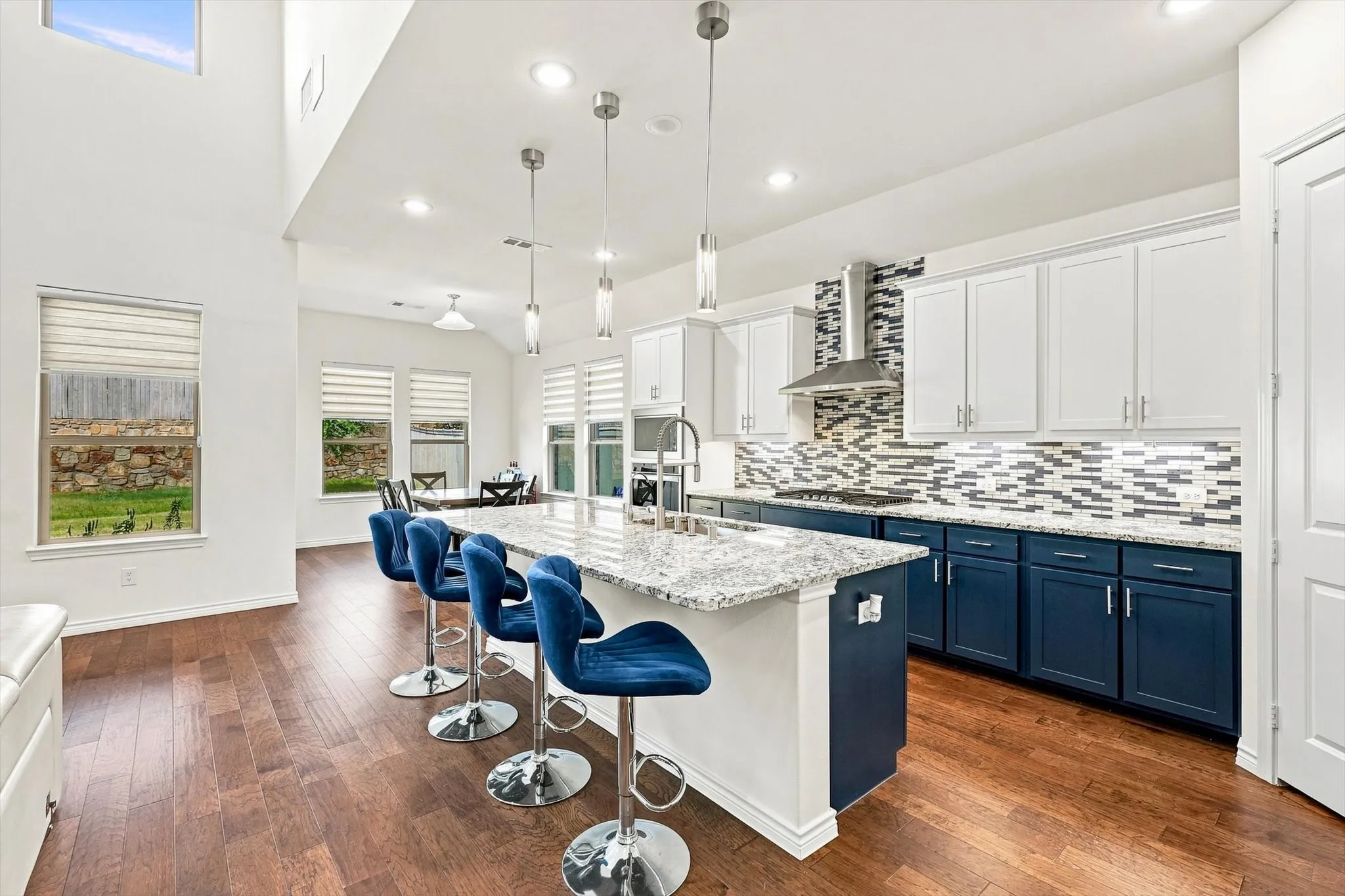 Open-concept kitchen with a large island featuring a stone countertop, wood-finish flooring, two-tone cabinetry, and stainless steel appliances
