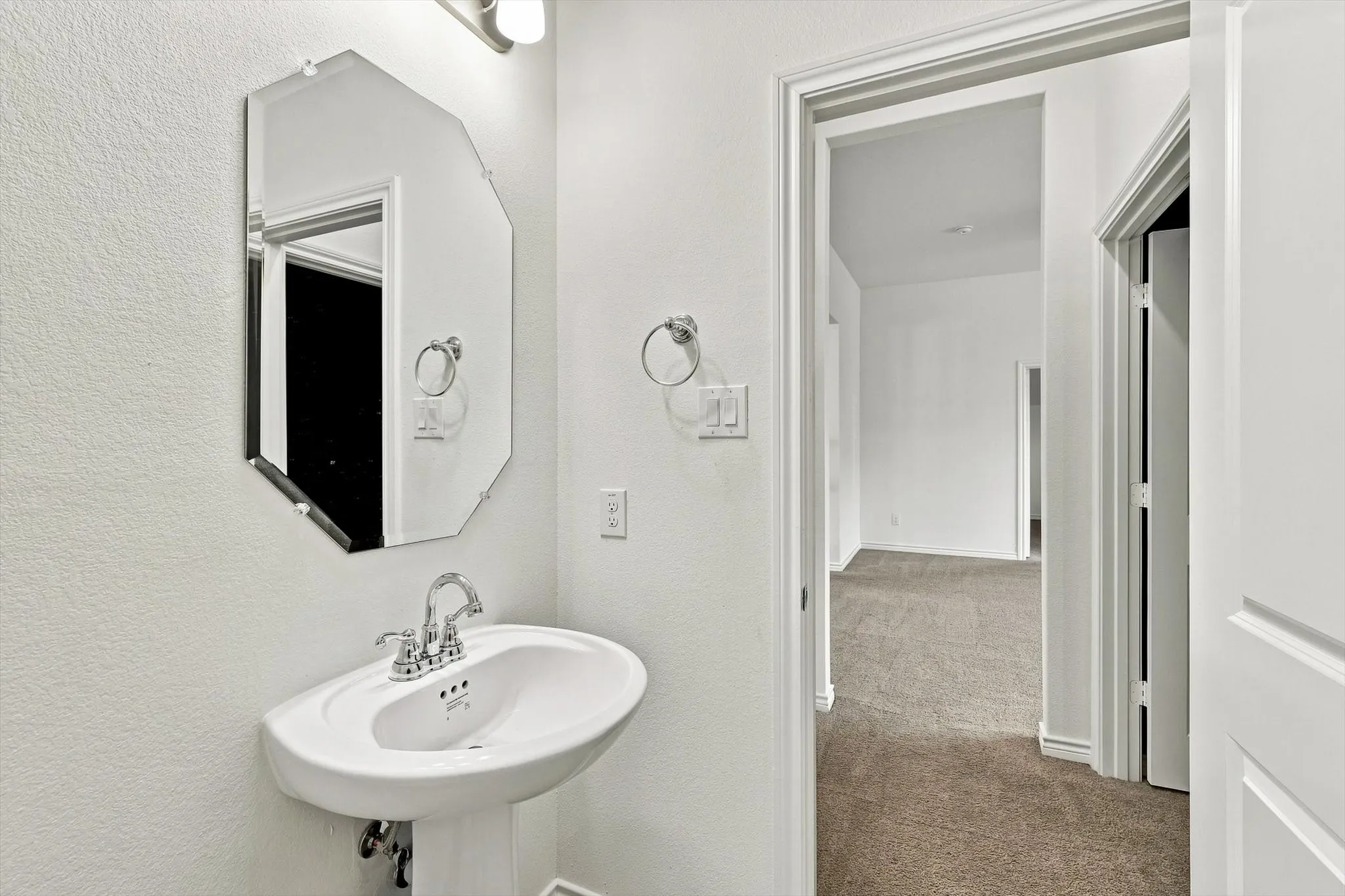 Pedestal sink with chrome faucet, octagonal frameless mirror, and overhead vanity light