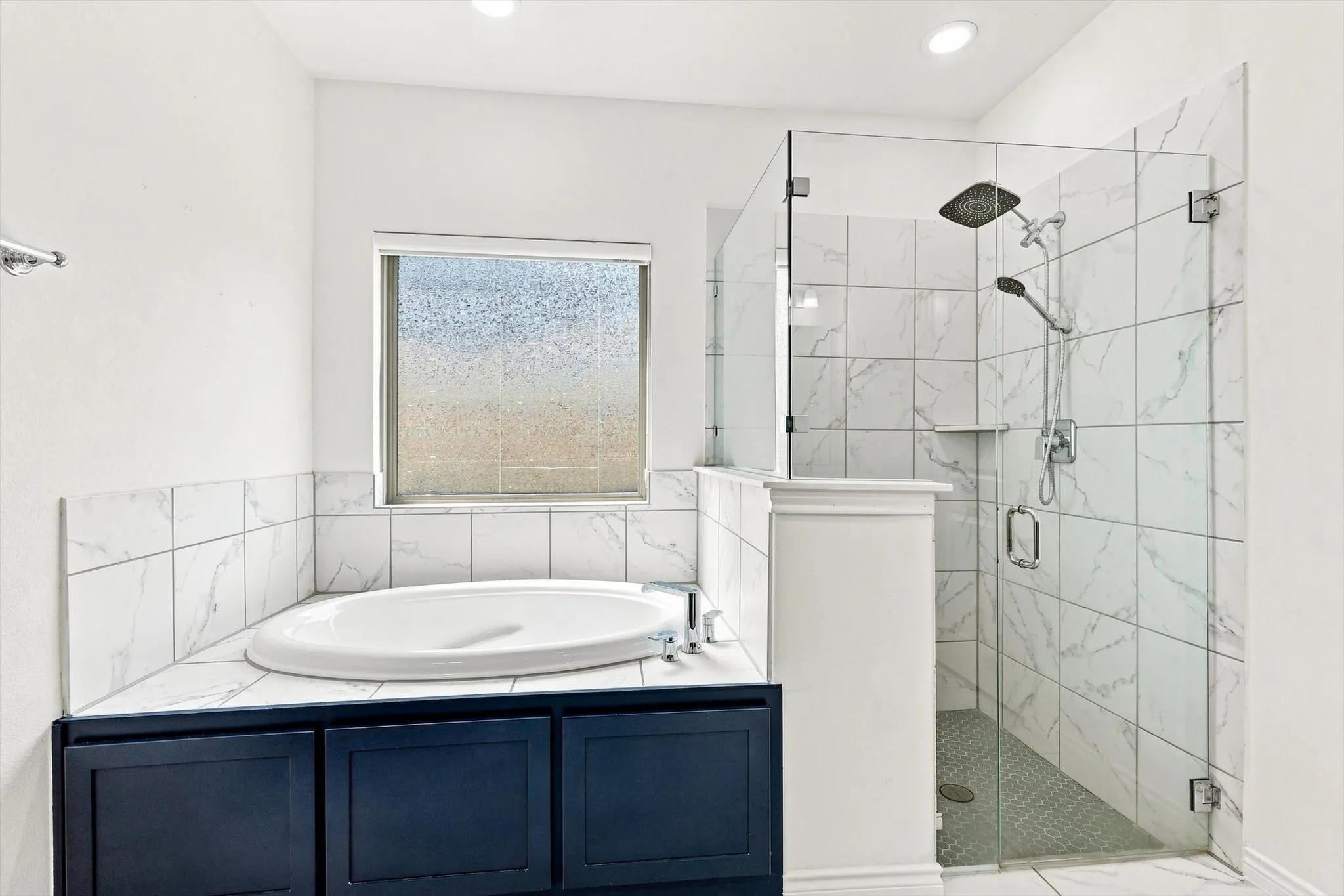 Corner soaking tub with dark cabinetry and surrounding tile, alongside a frameless glass shower enclosure with a rain shower head and handheld spray