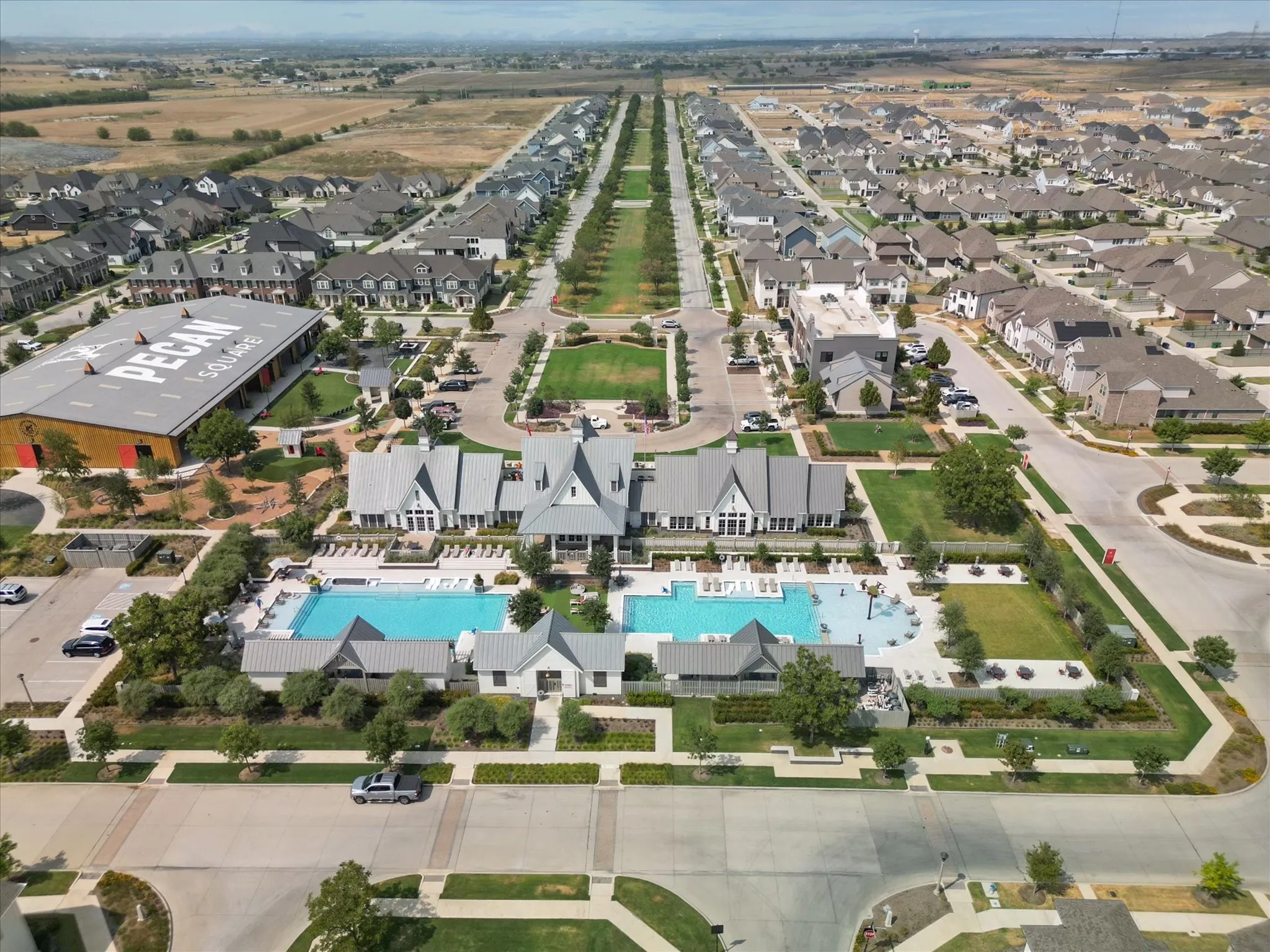 Expansive community featuring multiple residential structures, two large swimming pools, manicured green spaces, and a prominent community building