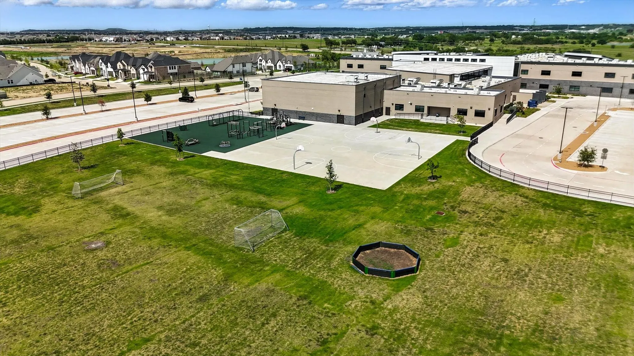 Expansive green space featuring two soccer goals, a playground with safety surfacing, and a paved basketball court