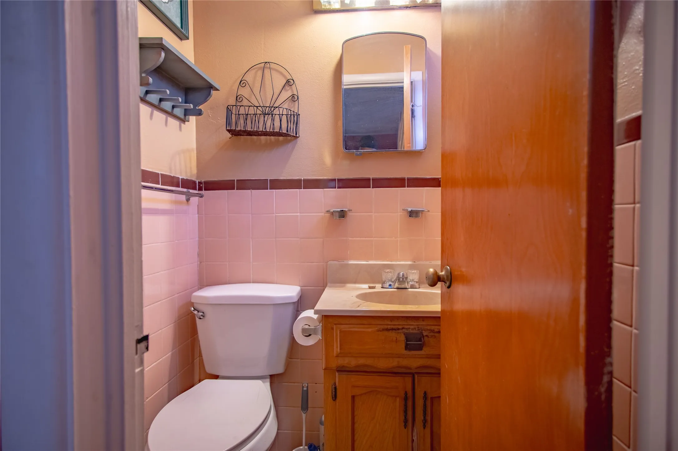 Bathroom featuring a toilet, a single vanity with an integrated sink, a wood-finish cabinet, and pink wall tiling