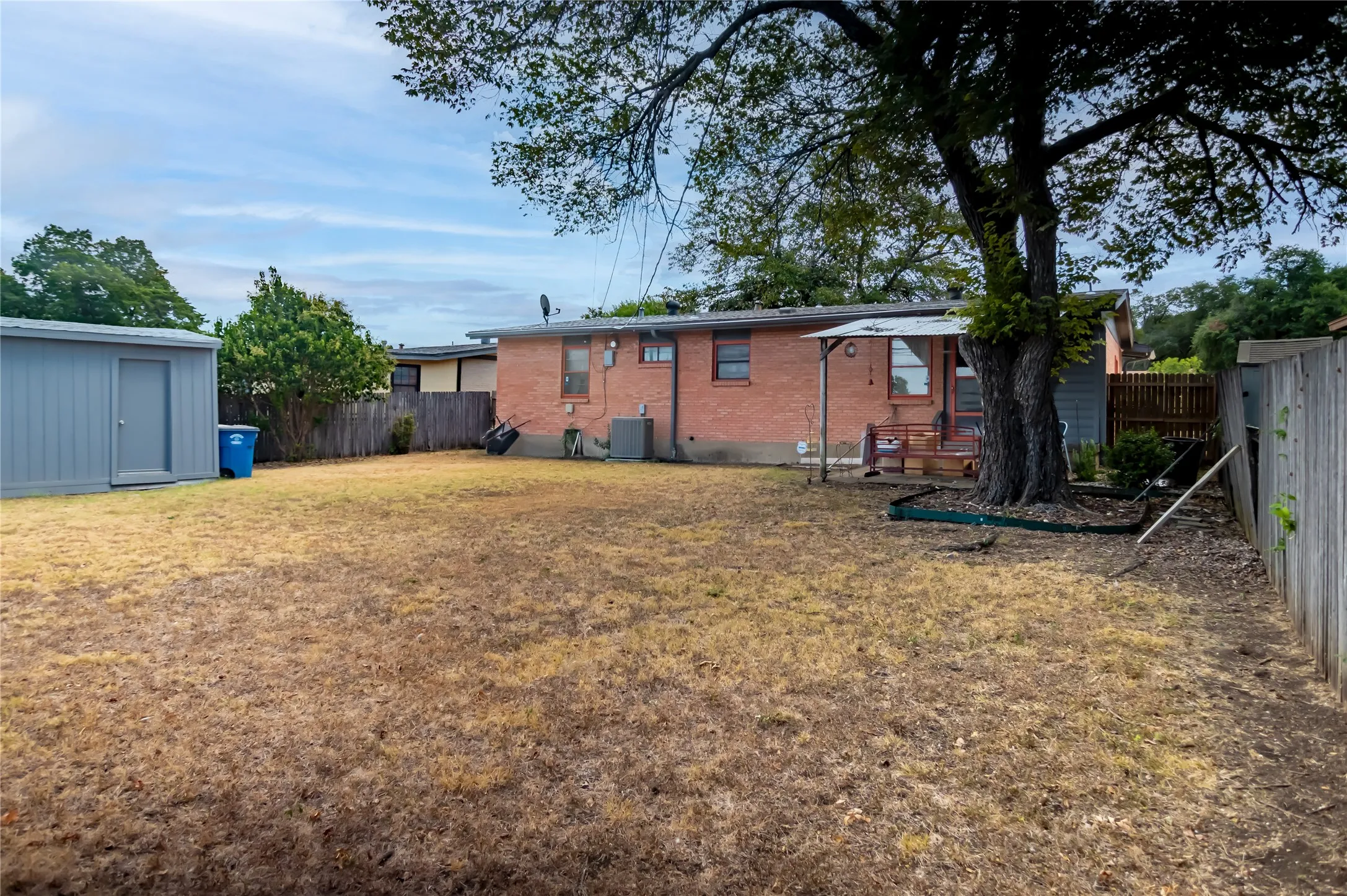 Expansive backyard featuring a mature tree, privacy fencing, a brick-clad exterior, and a detached storage shed