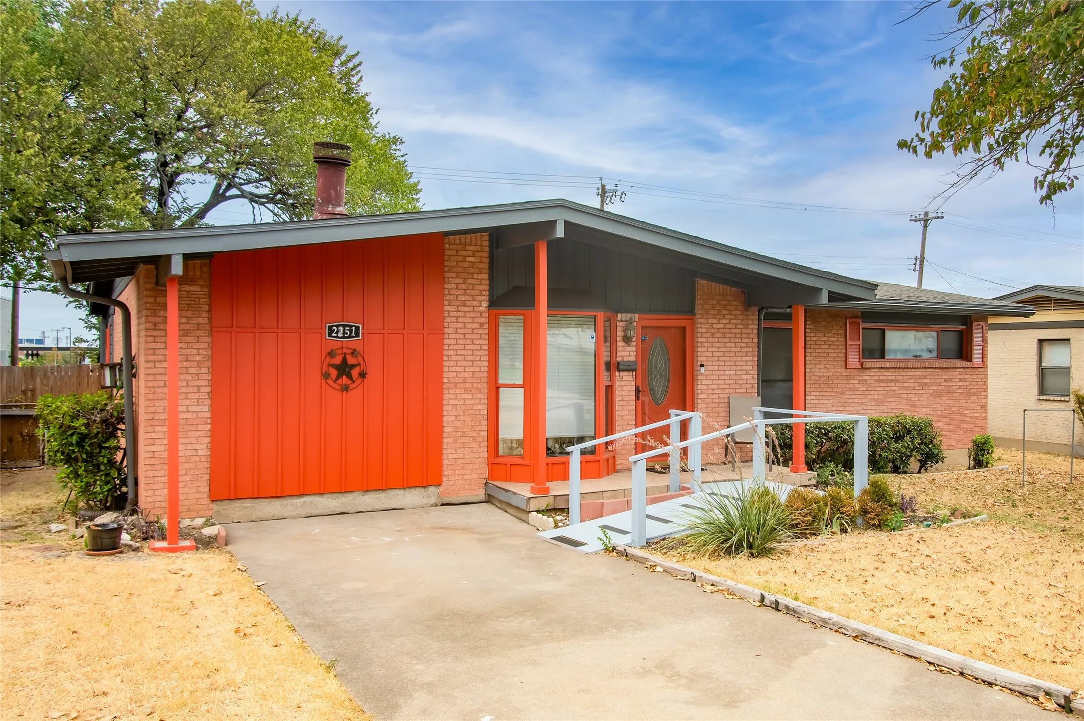 Brick exterior with a prominent orange garage door, an entry ramp, and an extended carport roofline