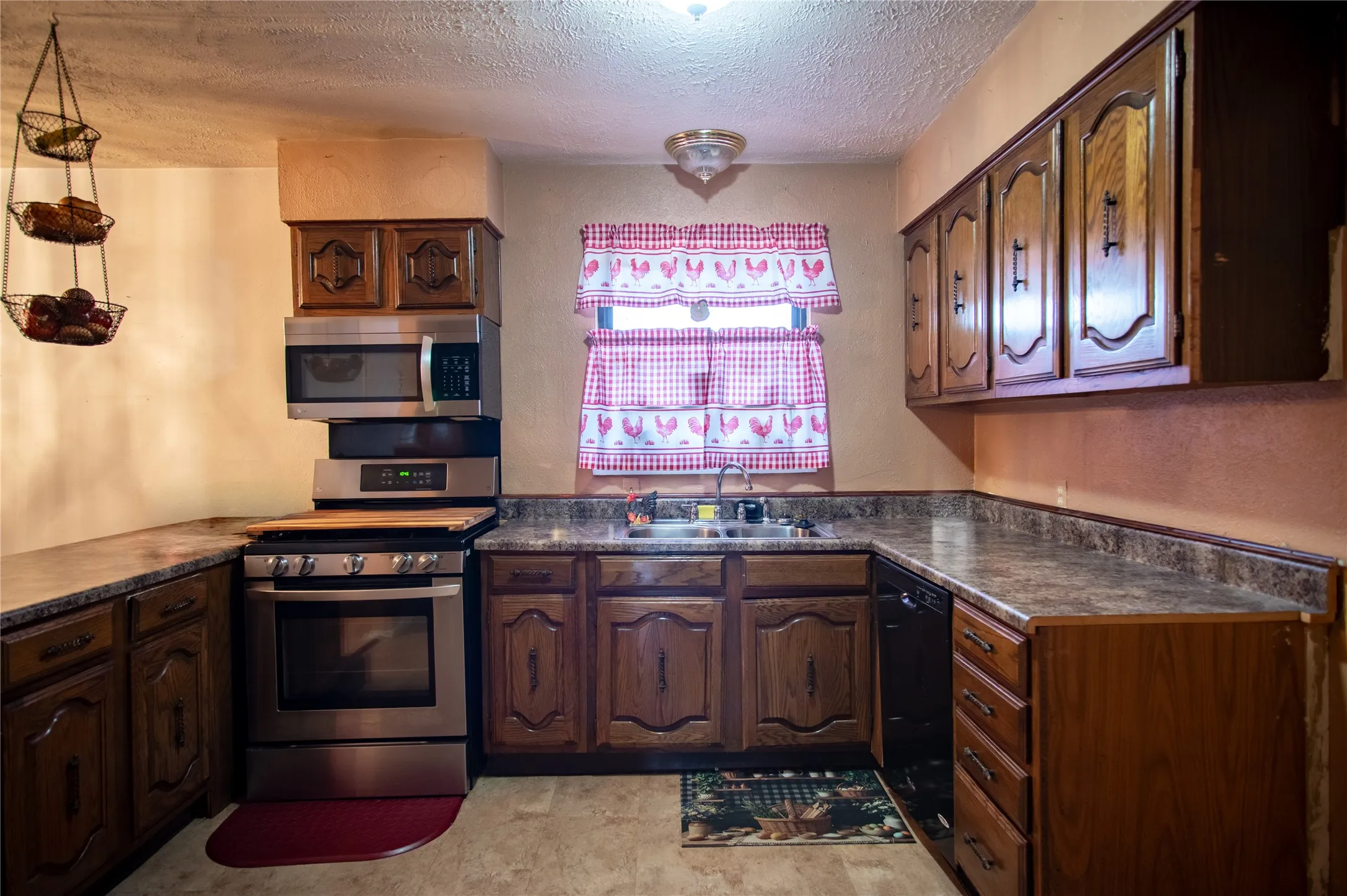 U-shaped kitchen layout featuring wood cabinetry, stainless steel oven with overhead microwave, and a double-basin sink
