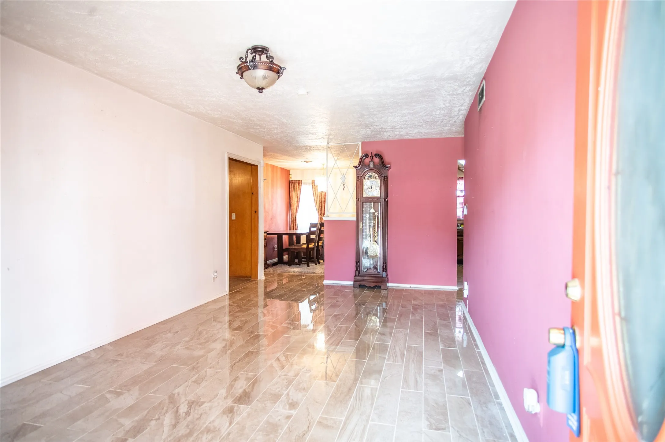 Hallway with polished tile flooring, ceiling-mounted light fixture, and wood-finish interior door