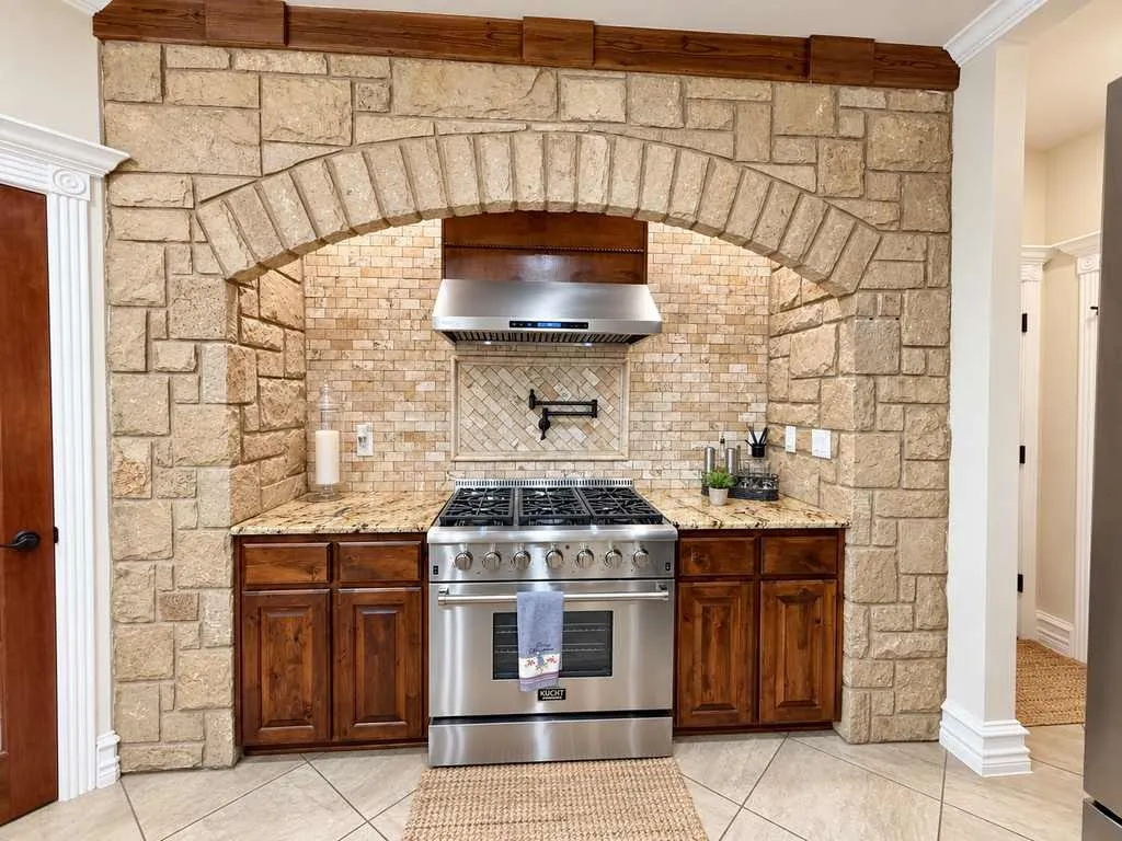 Stone-accented cooking area with gas range and pot filler.