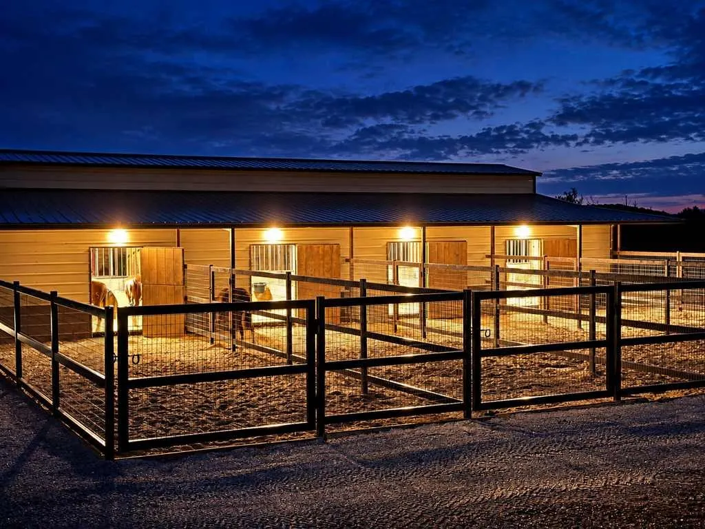 Evening view of the illuminated horse barn and fenced enclosure.