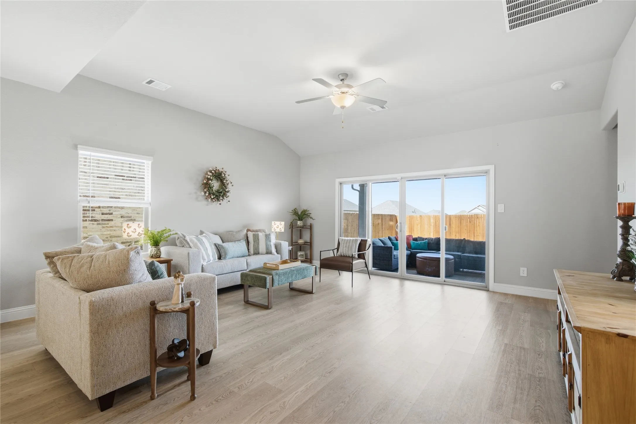 Vaulted ceilings, wood-finish flooring, ceiling fan, sliding glass door, and backyard patio