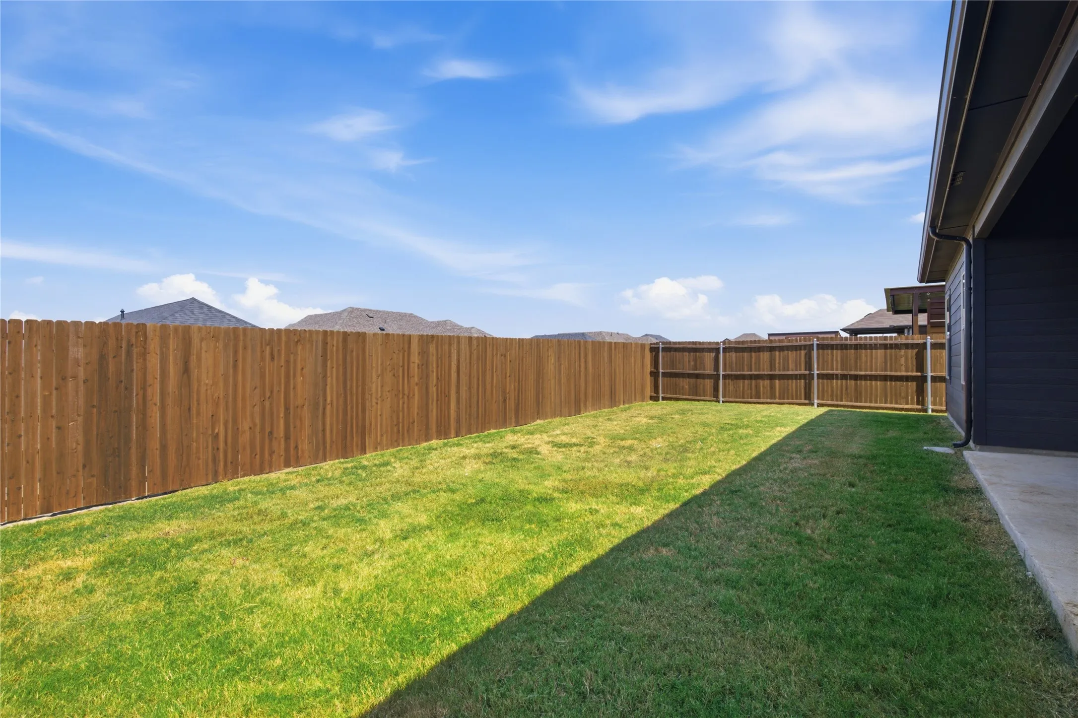 Expansive backyard featuring a privacy fence, manicured lawn, and concrete patio