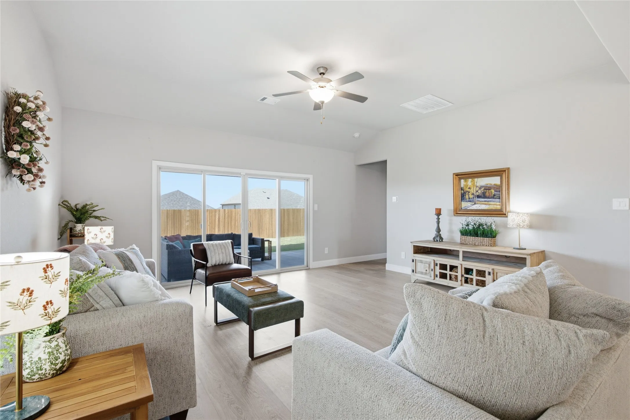 Spacious living area featuring light wood-finish flooring, a contemporary ceiling fan, and sliding glass doors providing access to the backyard