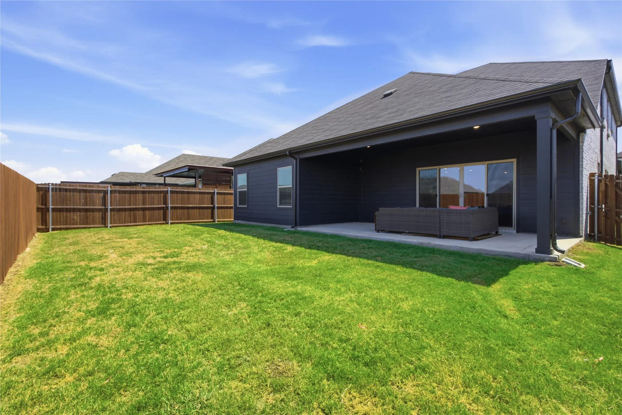 Expansive backyard featuring a manicured lawn, full privacy fencing, and a covered patio with recessed lighting