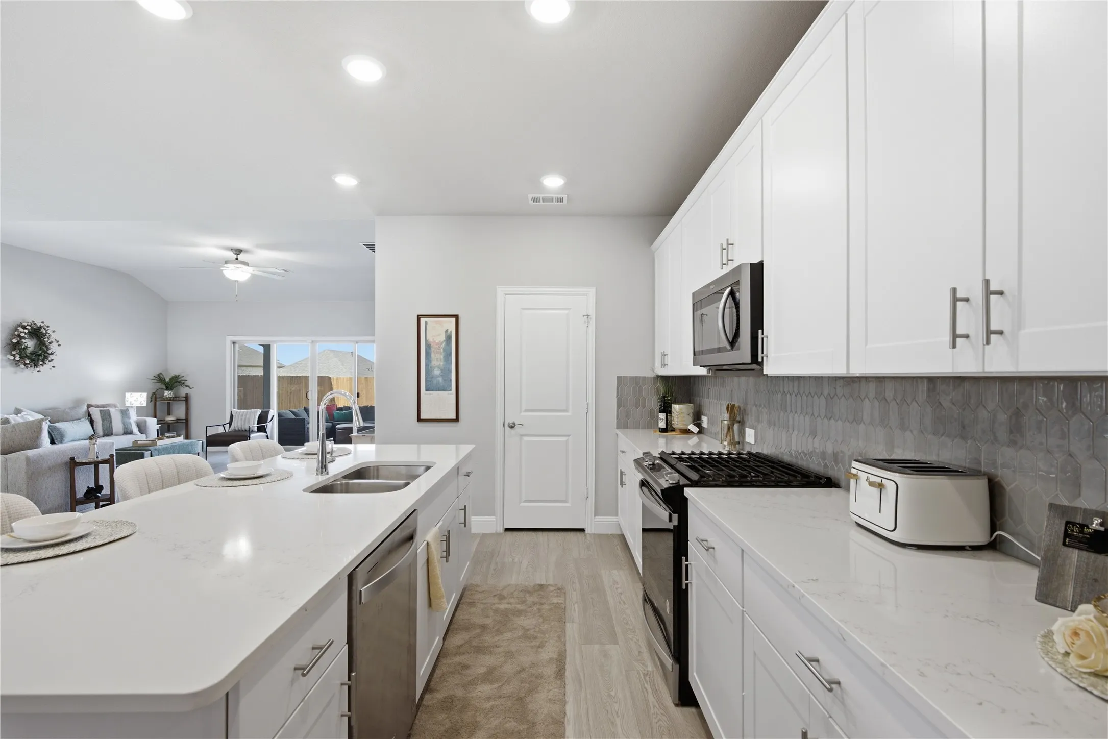 Kitchen featuring white cabinetry, stainless steel appliances, a large island with an undermount sink, and light-colored countertops
