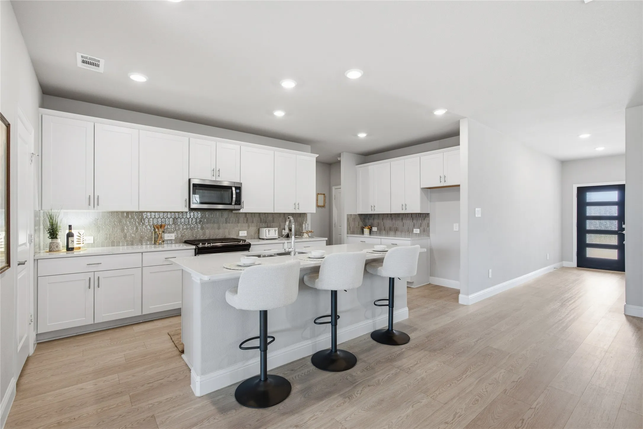 White shaker cabinetry with stainless steel hardware, mosaic tile backsplash, central island, wood-finish flooring, and recessed lighting