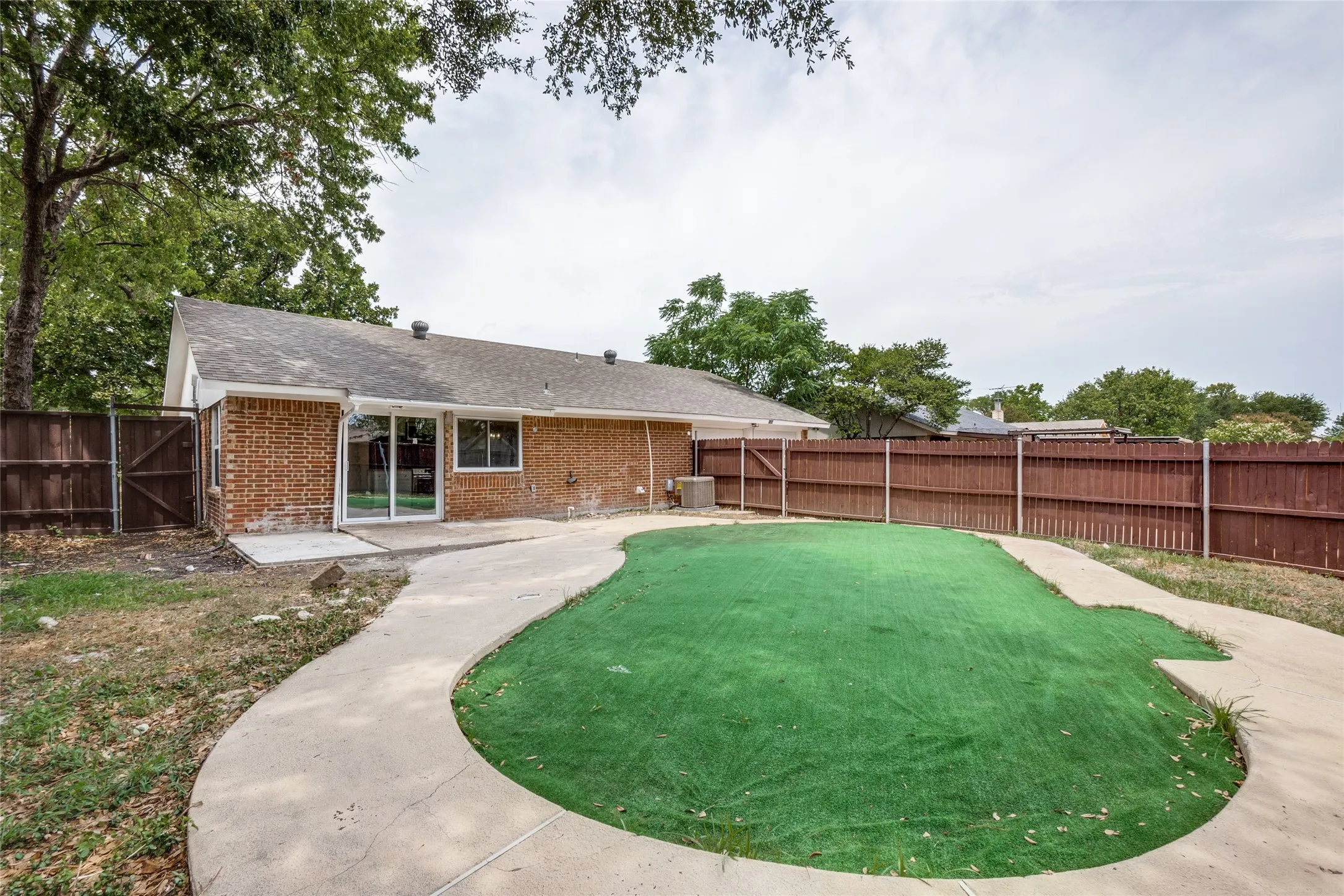 Brick exterior, sliding glass door, paved patio, perimeter fencing, synthetic turf area