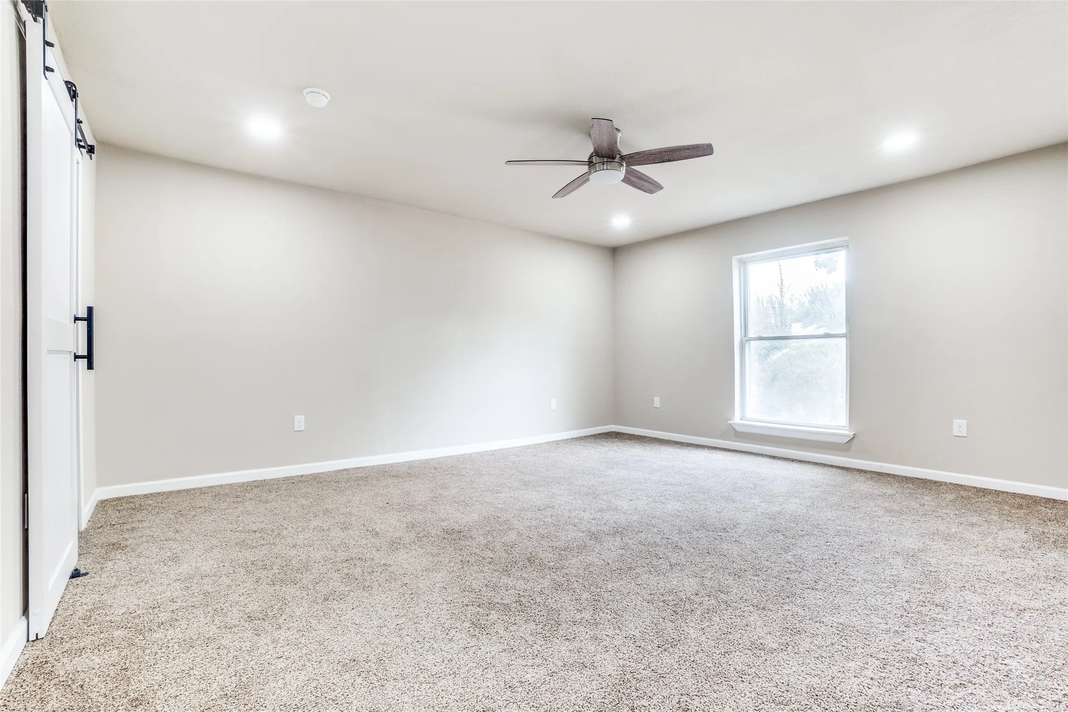 Spacious room featuring neutral carpet, a single window, and a ceiling fan with integrated lighting