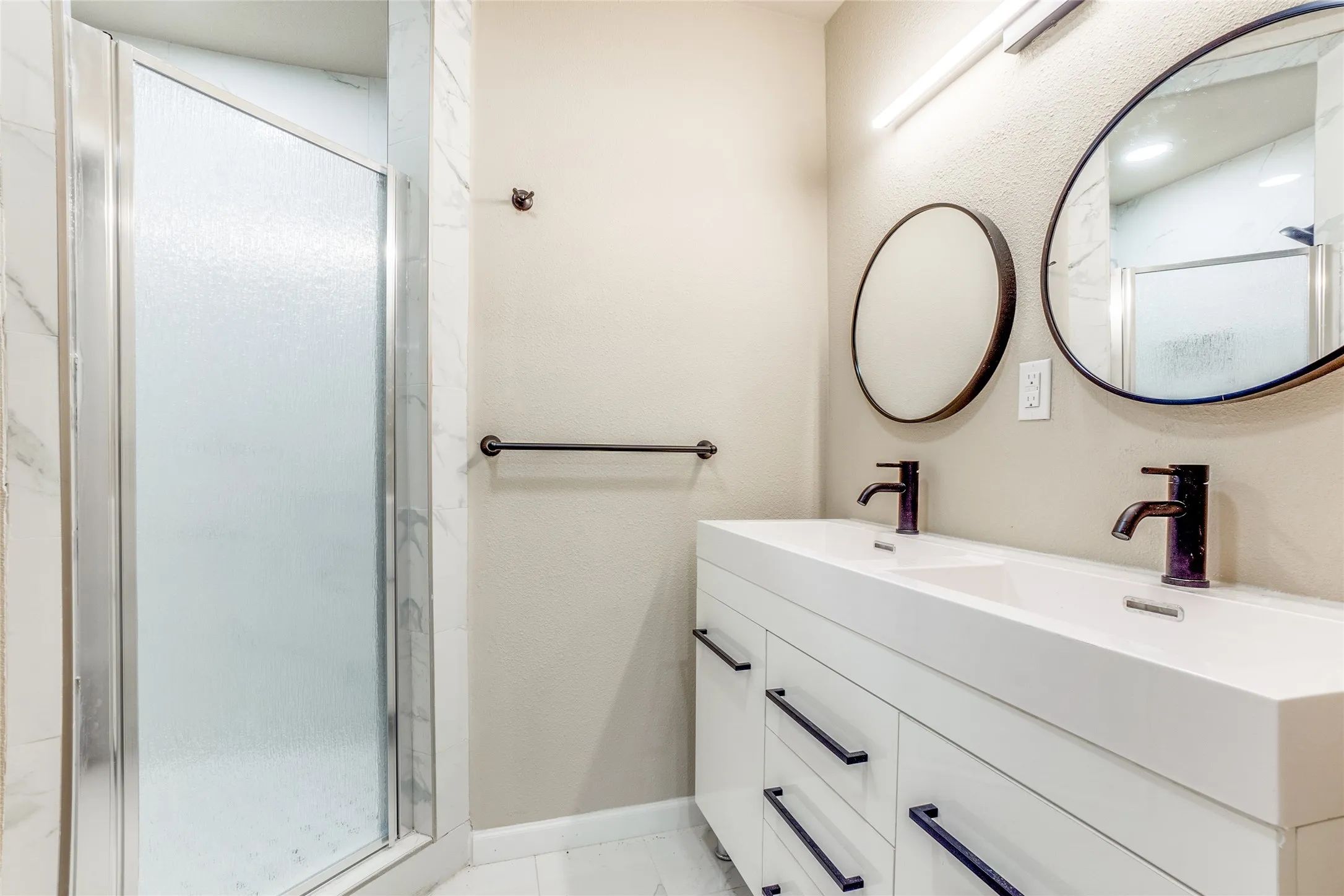 Dual vanity with integrated sinks and matte black fixtures, framed mirrors, and a glass-enclosed shower