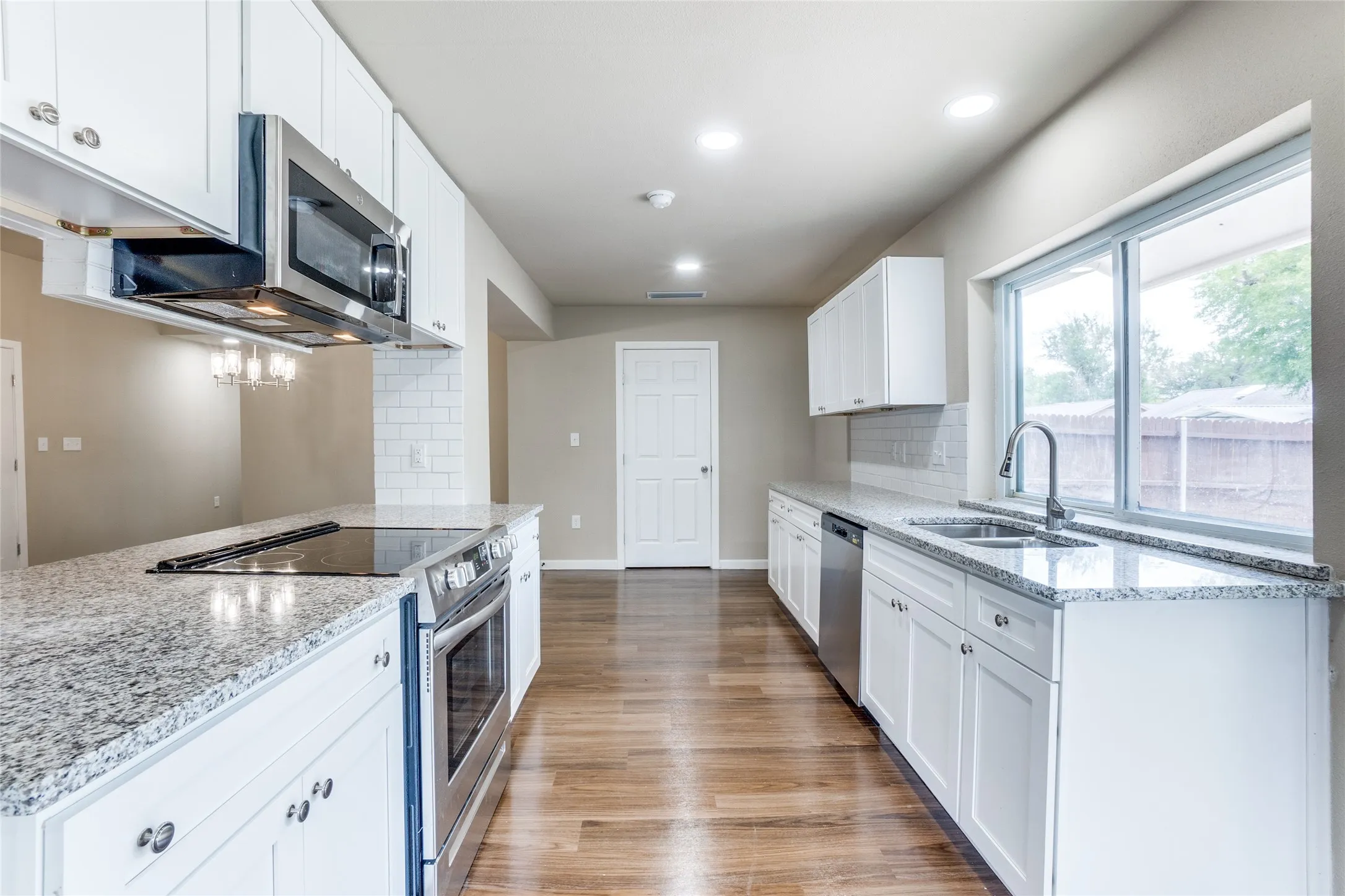Kitchen featuring white shaker-style cabinetry, stainless steel appliances, granite countertops, and wood-finish flooring